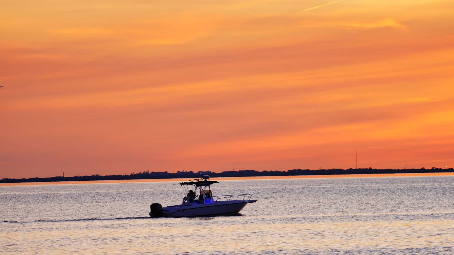 The vibrant skyline of downtown Tampa, Florida, is silhouetted against a colorful sunset sky of orange, pink, and purple hues. The modern skyscrapers are reflected in the smooth, tranquil water of Tampa Bay or the Hillsborough River.