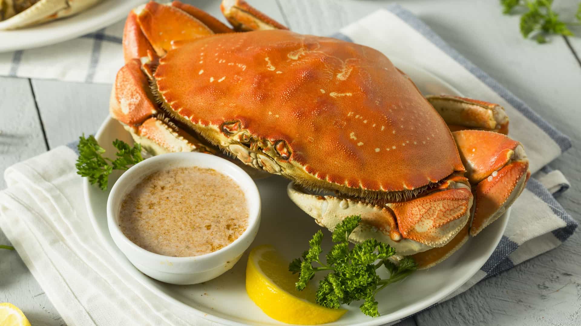  A freshly cooked, whole Dungeness crab, a popular seafood in Vancouver, British Columbia, is presented on a platter alongside a small bowl of melted butter for dipping. The crab is bright red and partially cracked, emphasizing its texture, suggesting a decadent, regional seafood meal.