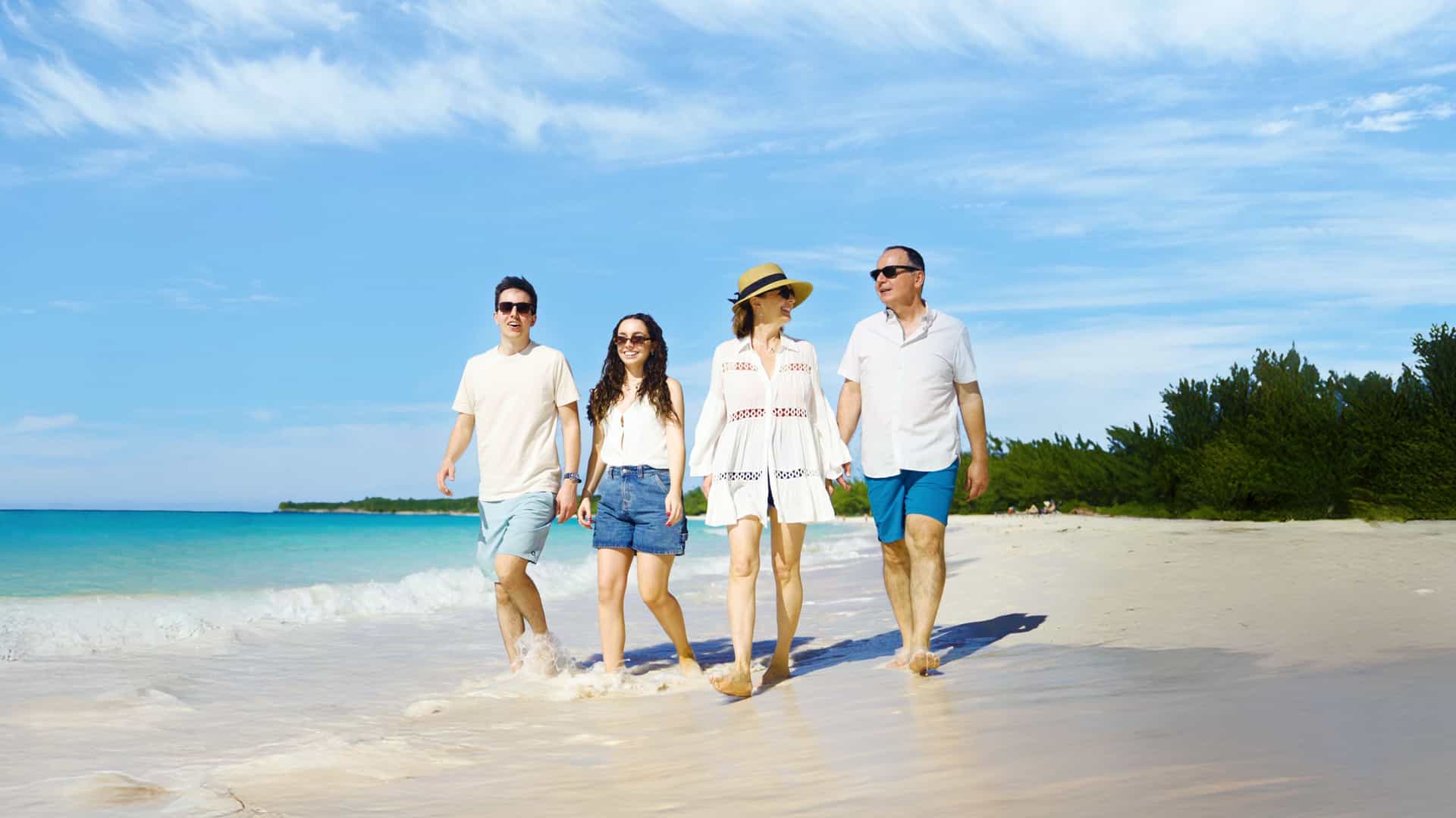 A family of four walks along the white-sand beach of Half Moon Cay in the Bahamas, enjoying a sunny Caribbean day on their Holland America Line cruise.
