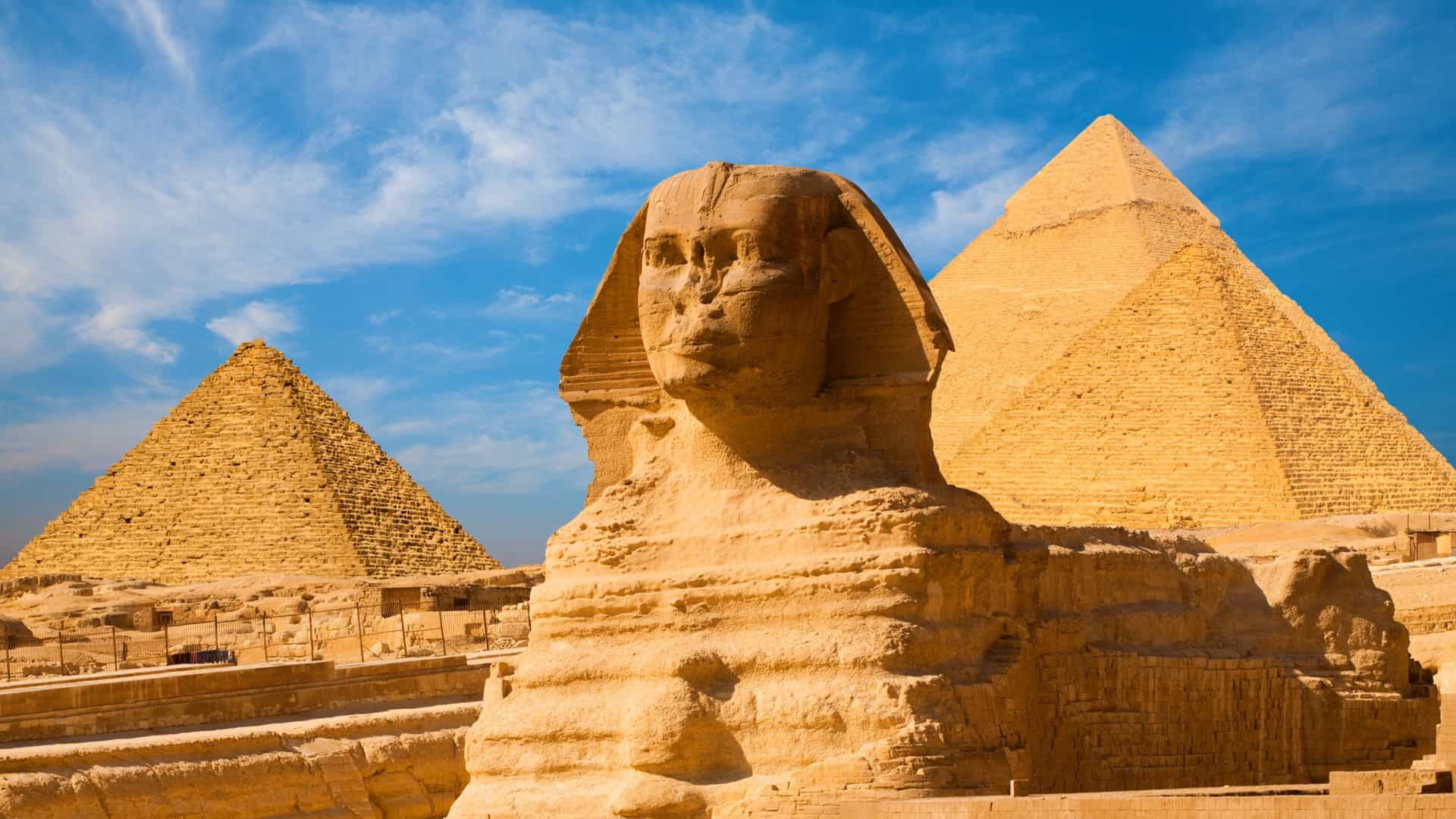 A close up image of the Sphinx with the Pyramids of Egypt and blue skies in the background.