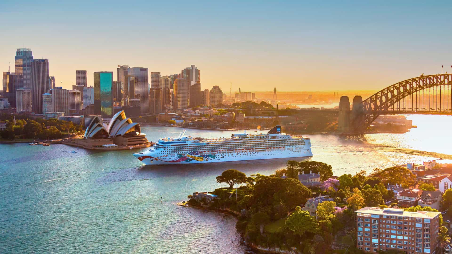 Norwegian Cruise Line Jewel ship arriving in Sydney Harbour, Australia, with the iconic Sydney Opera House and Harbour Bridge at sunset.