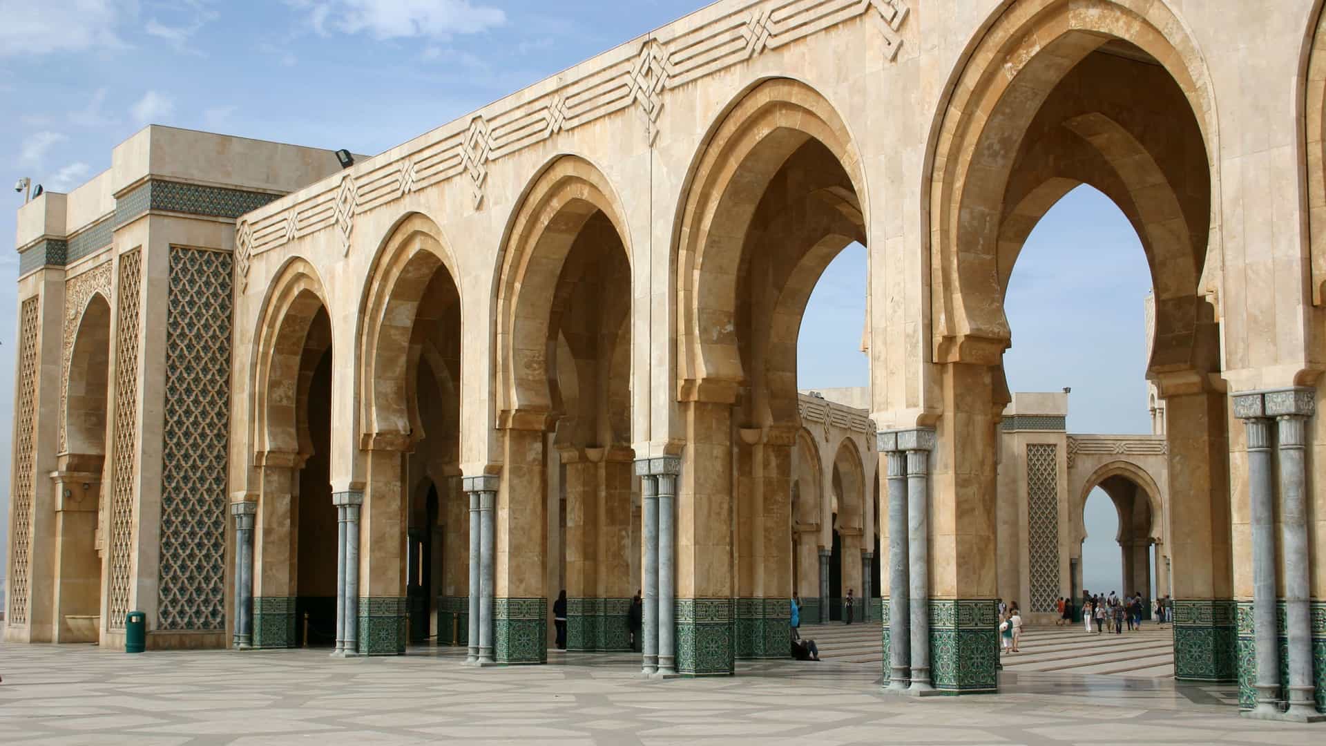 A view of the stunning architecture of the Hassan II Mosque in Casablanca, Morocco, featuring a long series of ornate stone arches and a spacious courtyard.