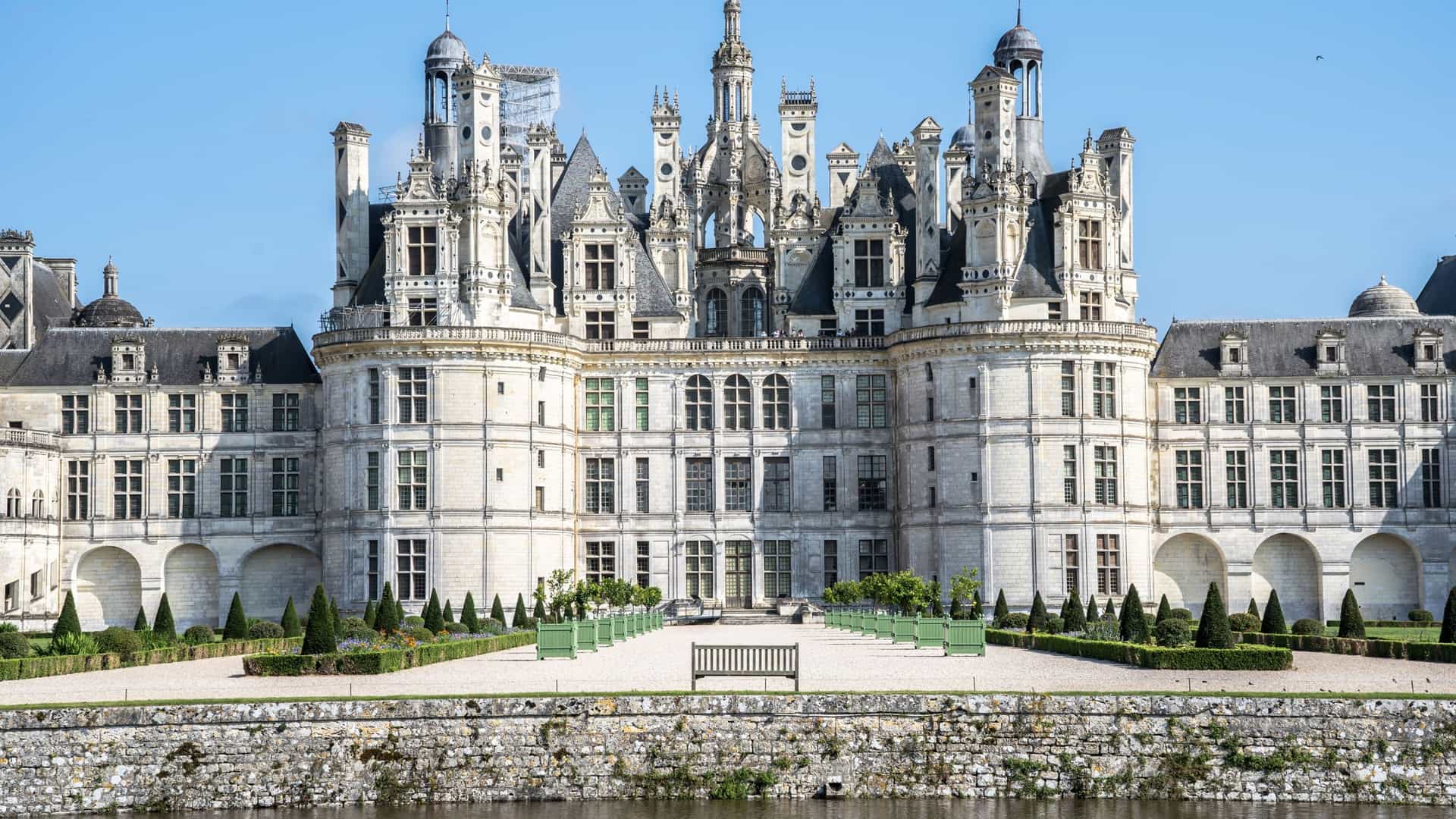 A front view of the magnificent Chateau de Chambord, with its Renaissance architecture, turrets, and ornate rooftop details, surrounded by manicured gardens and a serene moat in the Loire Valley, France.