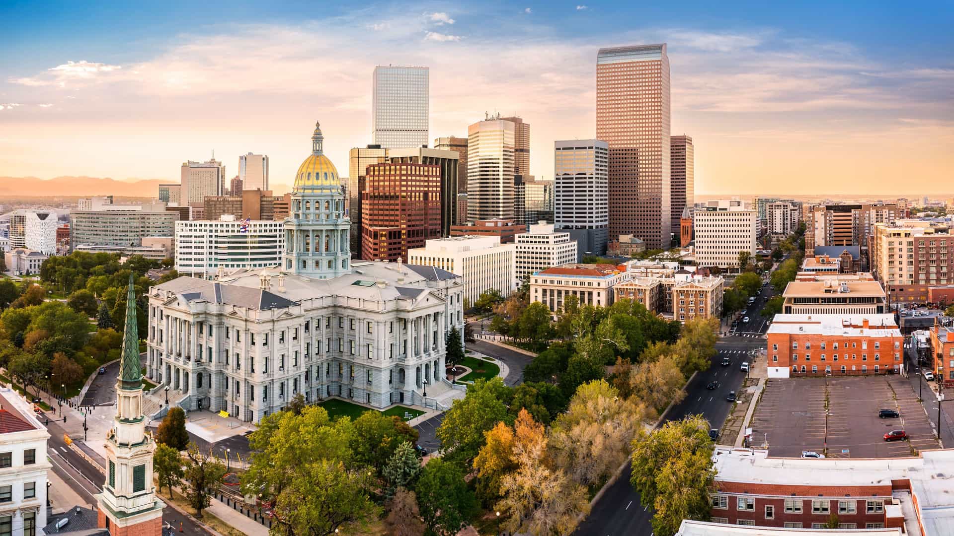 "A stunning panoramic shot of the Denver, Colorado, skyline, with the majestic gold-domed State Capitol building in the foreground and modern skyscrapers rising behind it, set against a beautiful sunset sky.  "