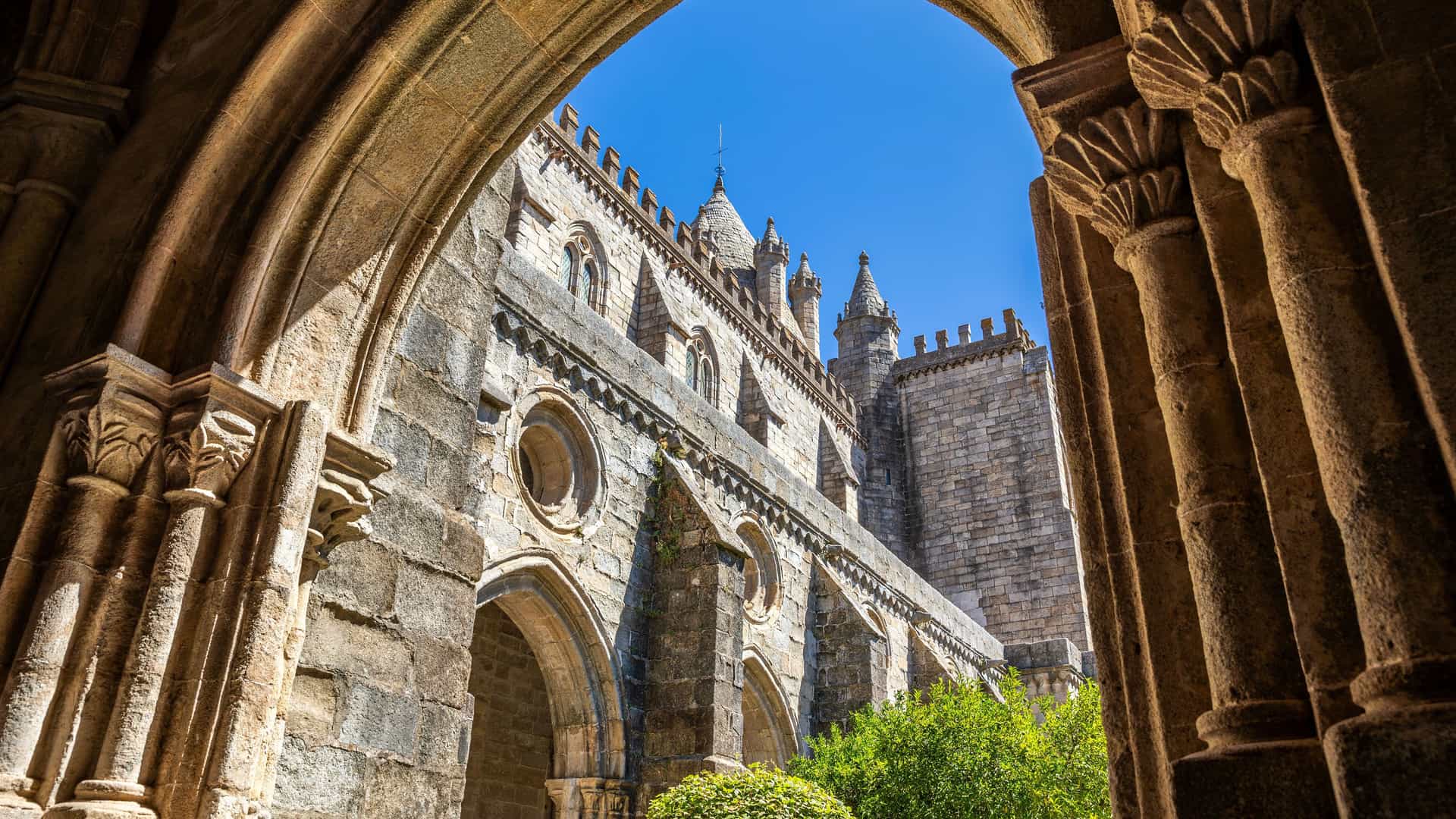 "A view from inside a stone archway of the historic Évora Cathedral in Portugal, with its robust Gothic architecture and a clear blue sky in the background.  "