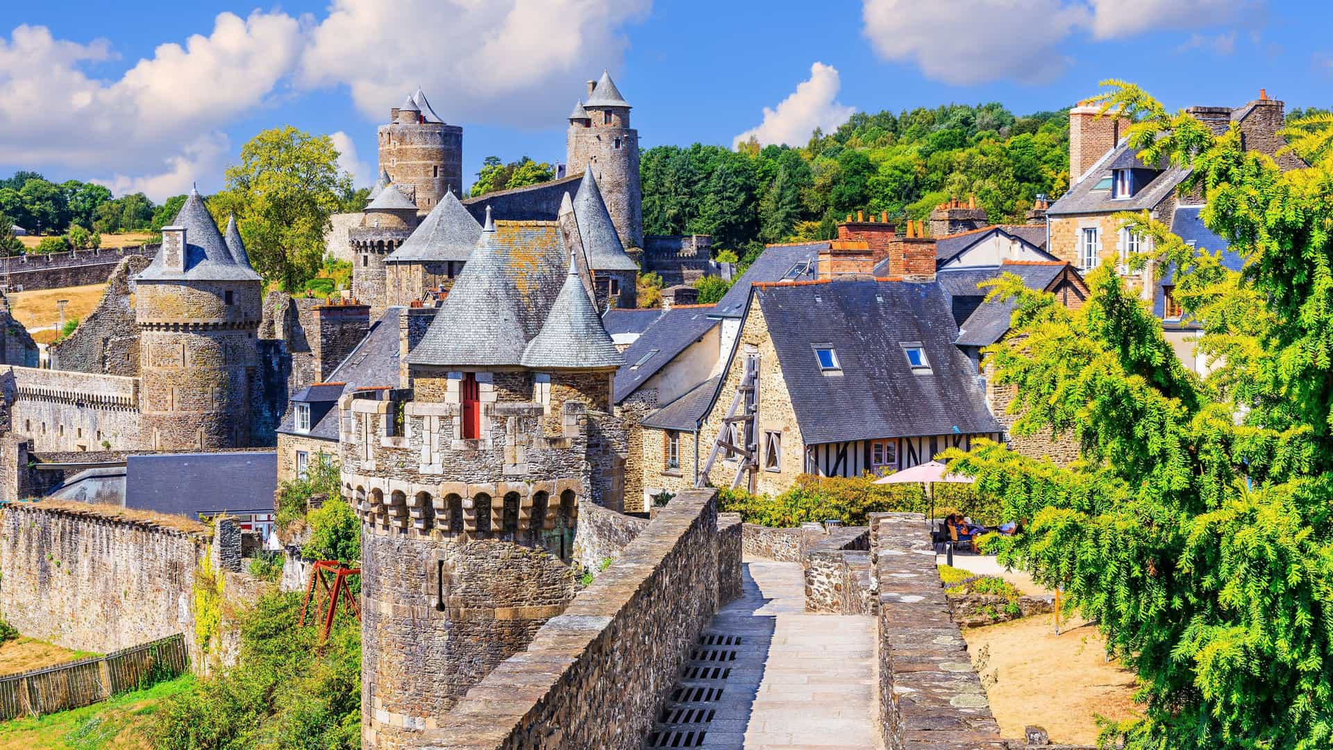 A vibrant, sunlit view of the medieval city of Fougères, France, showcasing the impressive stone castle walls, towers, and historic half-timbered houses.