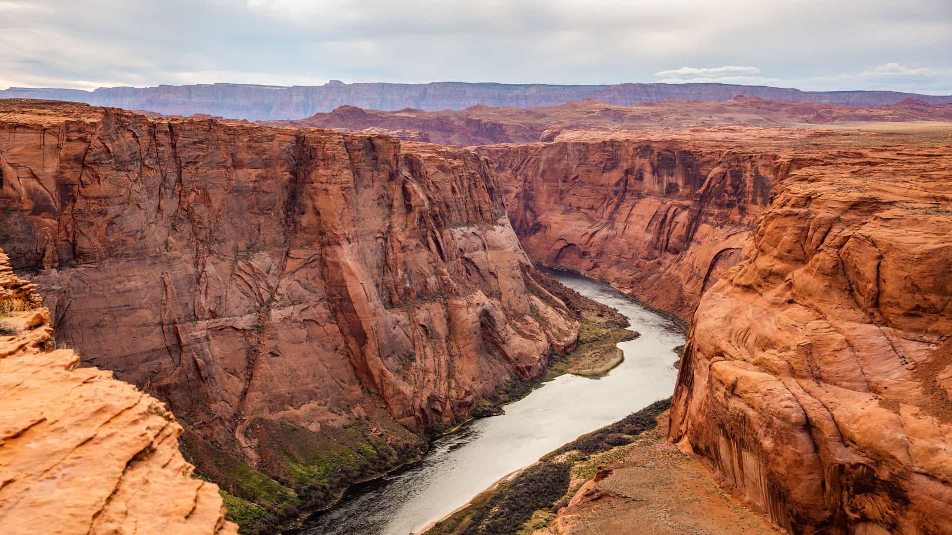 "A high-angle view of the iconic Horseshoe Bend at the Grand Canyon National Park, showcasing the Colorado River's sharp turn through the deep red and orange rock formations.  "