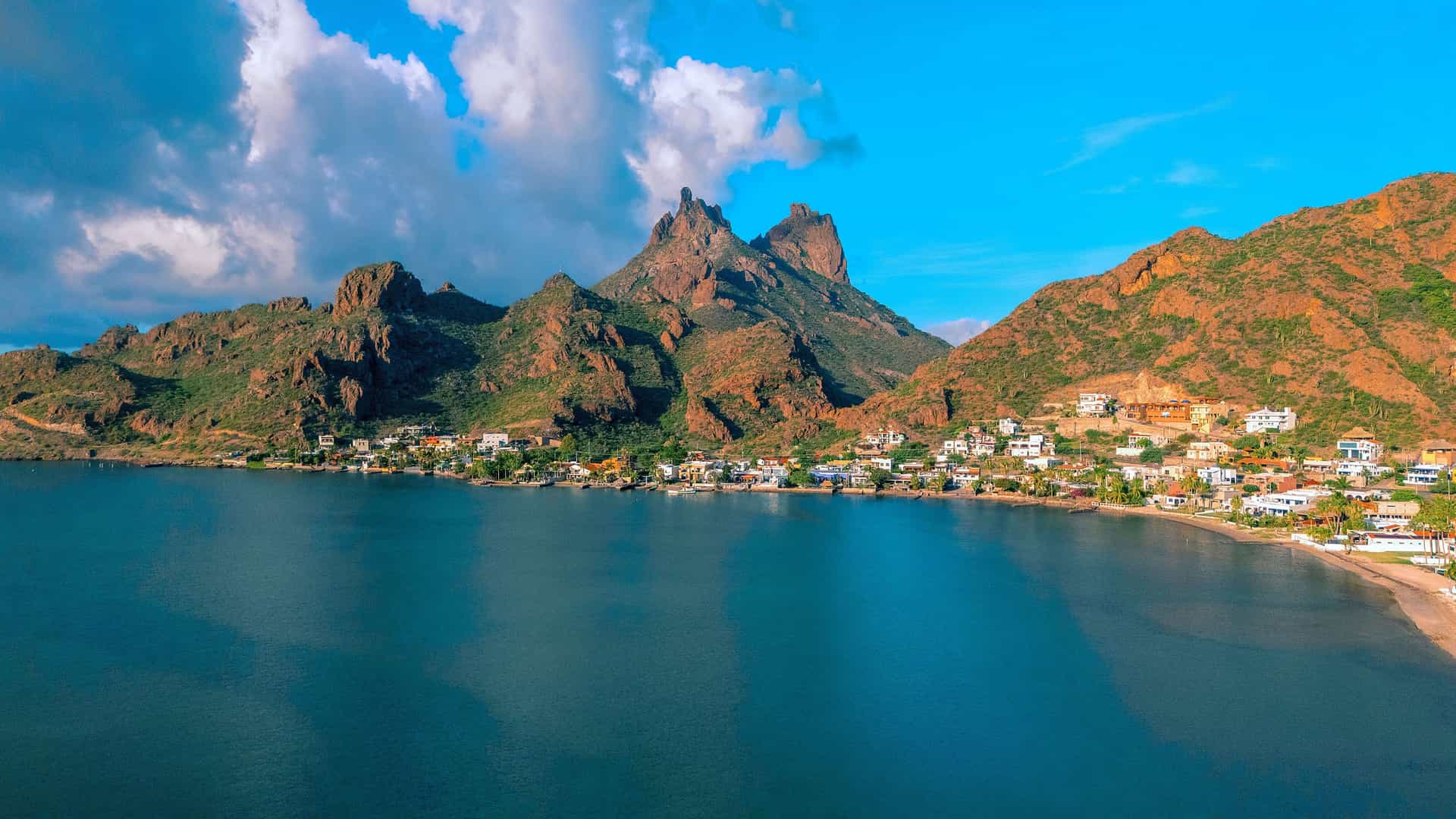 An aerial view of the scenic bay and coastal community in Guaymas, Mexico, with rugged mountains and a beautiful blue sky in the background.