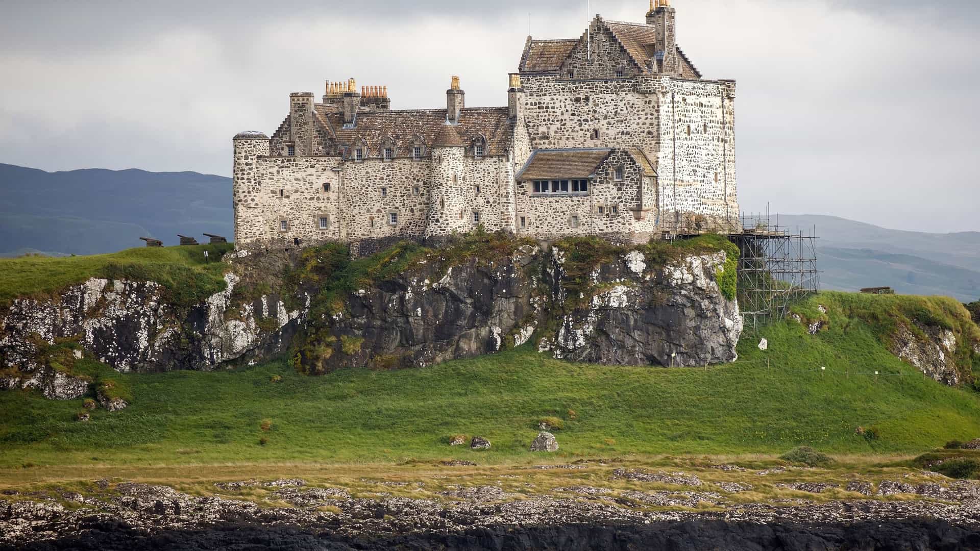 A scenic shot of Duart Castle, a historic stone fortress with a rugged exterior, situated on a green cliff overlooking the sea on the Isle of Mull.
