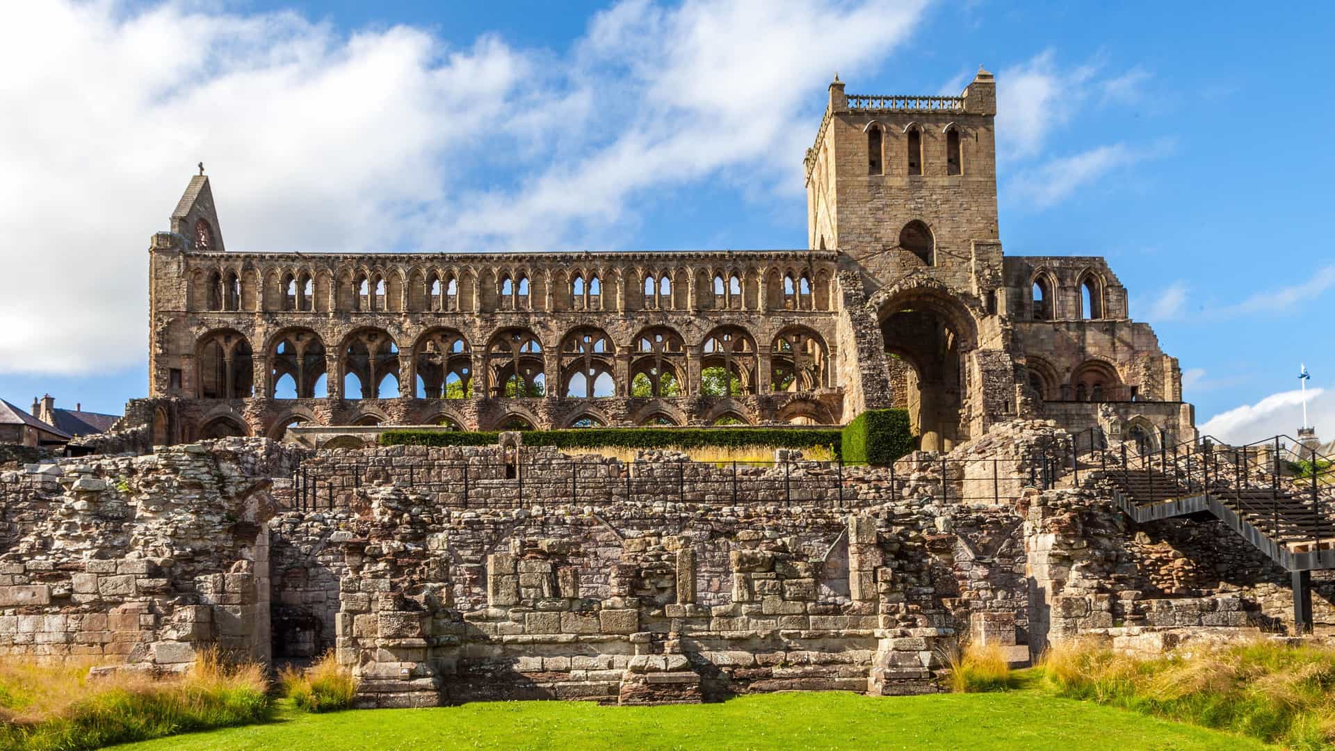 A scenic view of the magnificent ruins of Jedburgh Abbey, a historic medieval church, with its towering arches and stone walls against a bright blue sky.