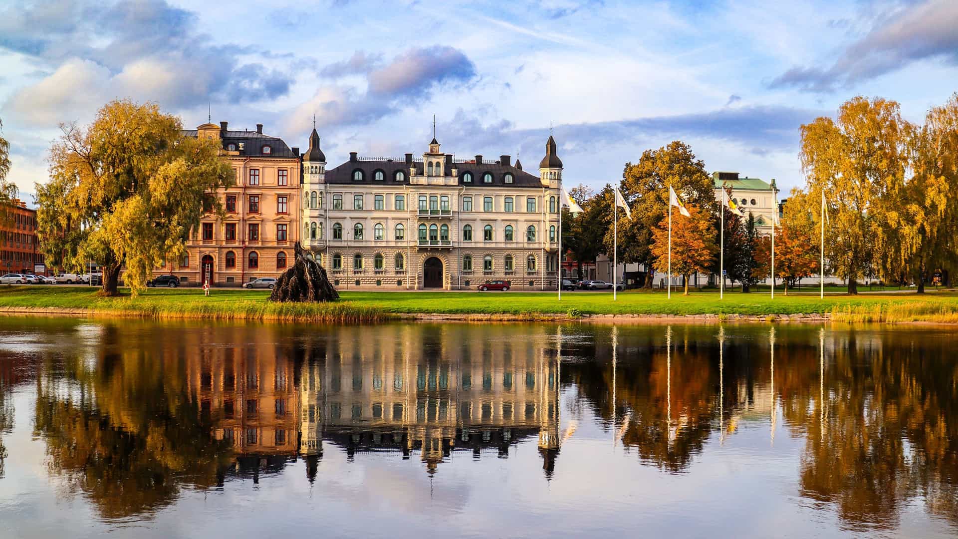 "A scenic autumn shot of the historic Värmlands Museum, a large white building with a castle-like design, reflecting beautifully in the waters of the Klarälven River in Karlstad, Sweden.  "