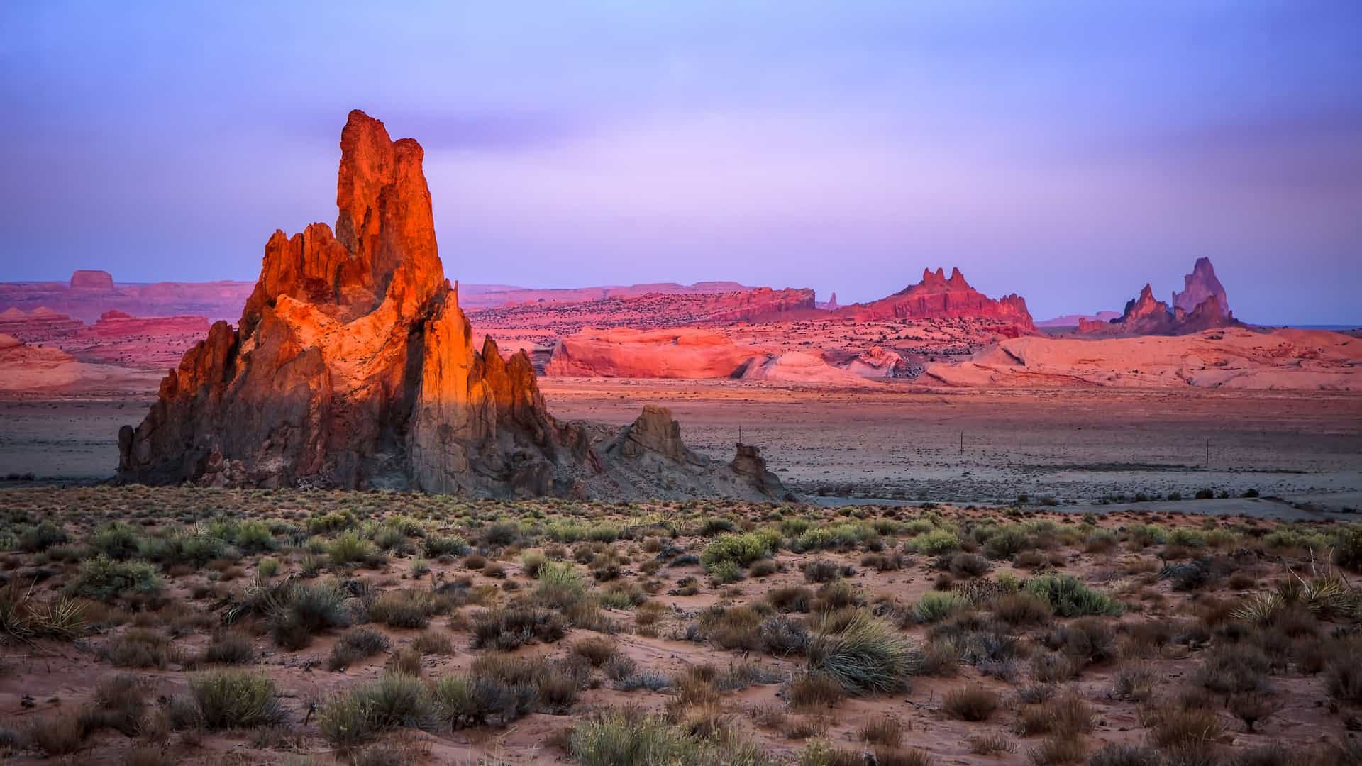 "A beautiful golden-hour shot of Monument Valley, near Kayenta, Arizona, with a striking red rock formation in the foreground and the expansive, arid desert landscape under a colorful sky.  "