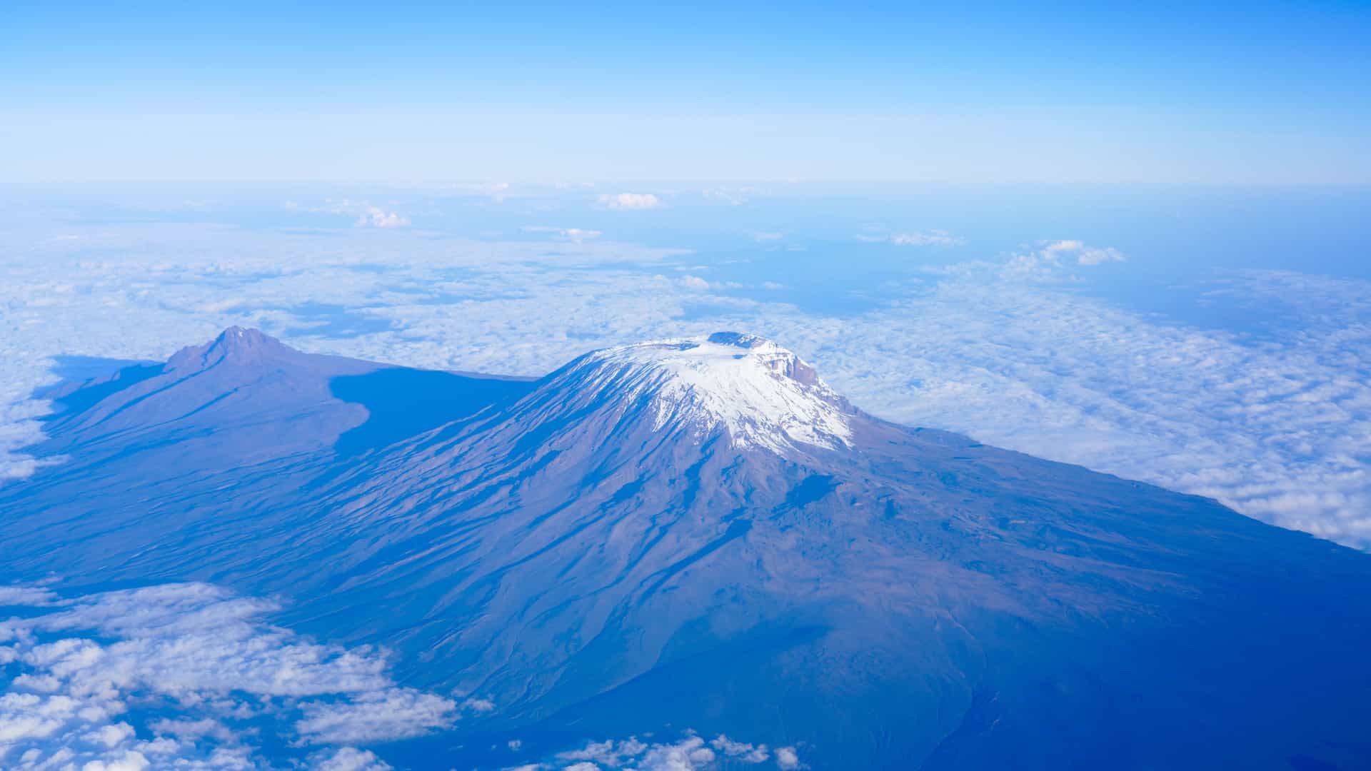 An aerial view of the snow-capped peak of Mount Kilimanjaro rising above a sea of clouds, a breathtaking landscape near the Kilimanjaro International Airport.