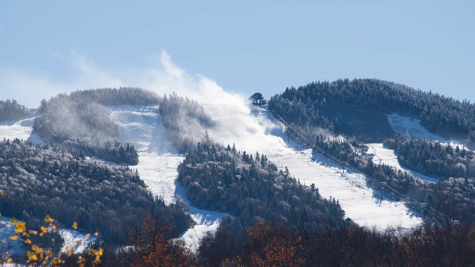 "A snowy scene of the Killington ski resort in Vermont, showing a ski lift ascending a snow-covered mountain with snow machines blowing artificial snow onto the trails.  "