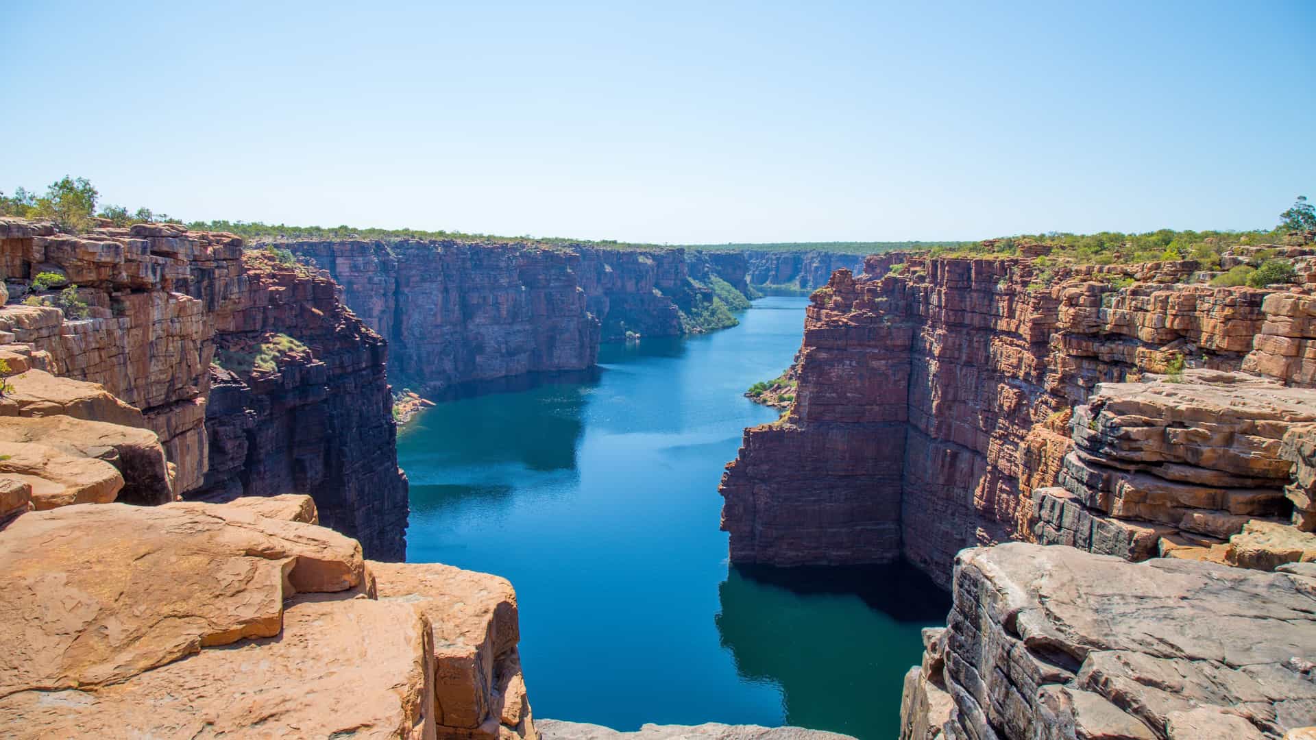 A breathtaking view of the King George River in Western Australia, surrounded by massive, orange-red sandstone cliffs with a calm, blue river running through the gorge.
