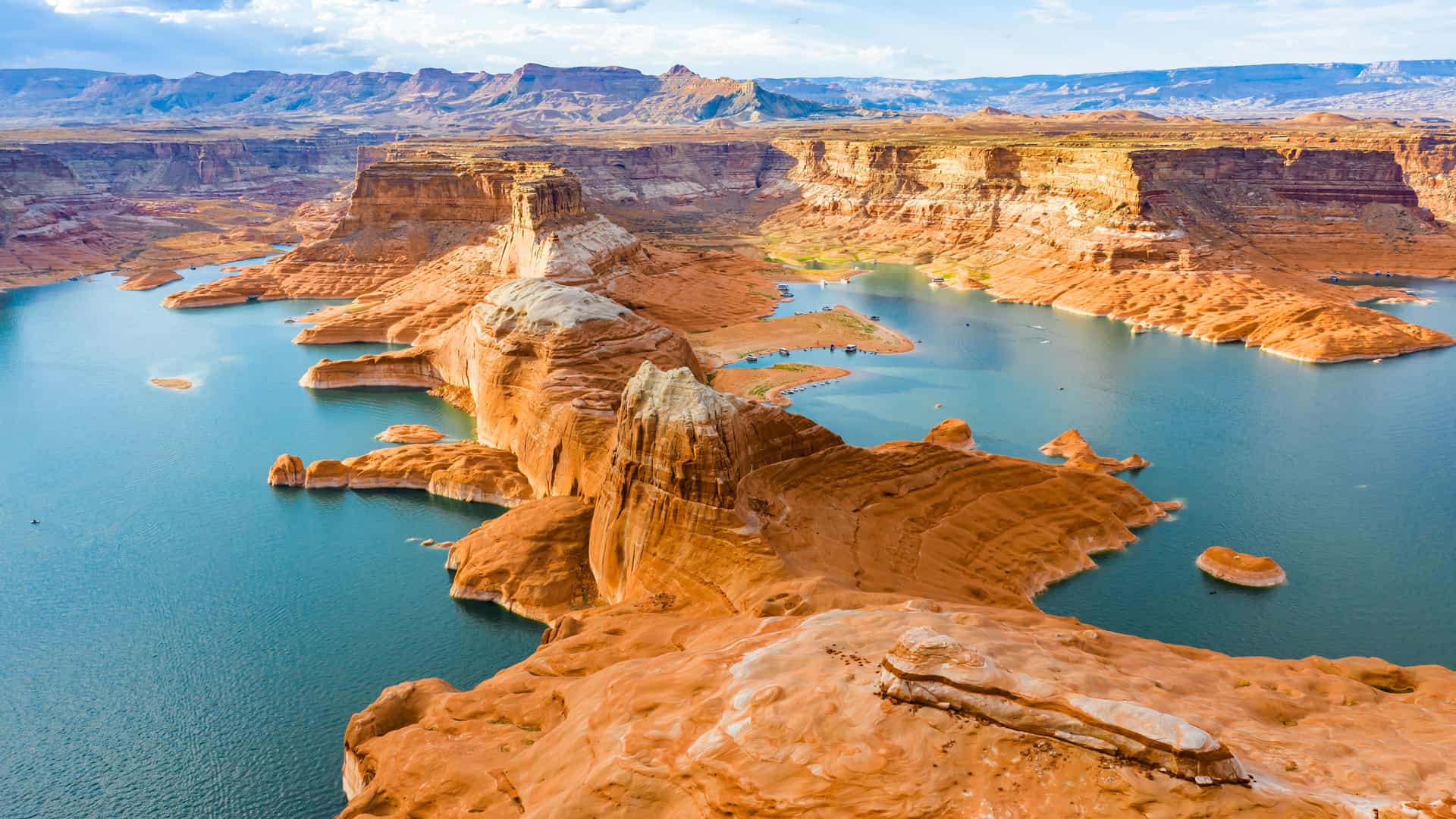 "An aerial panoramic shot of Lake Powell, a beautiful man-made reservoir in Utah, showcasing its vibrant blue waters and the stunning contrast of the red sandstone cliffs and unique rock formations.  "