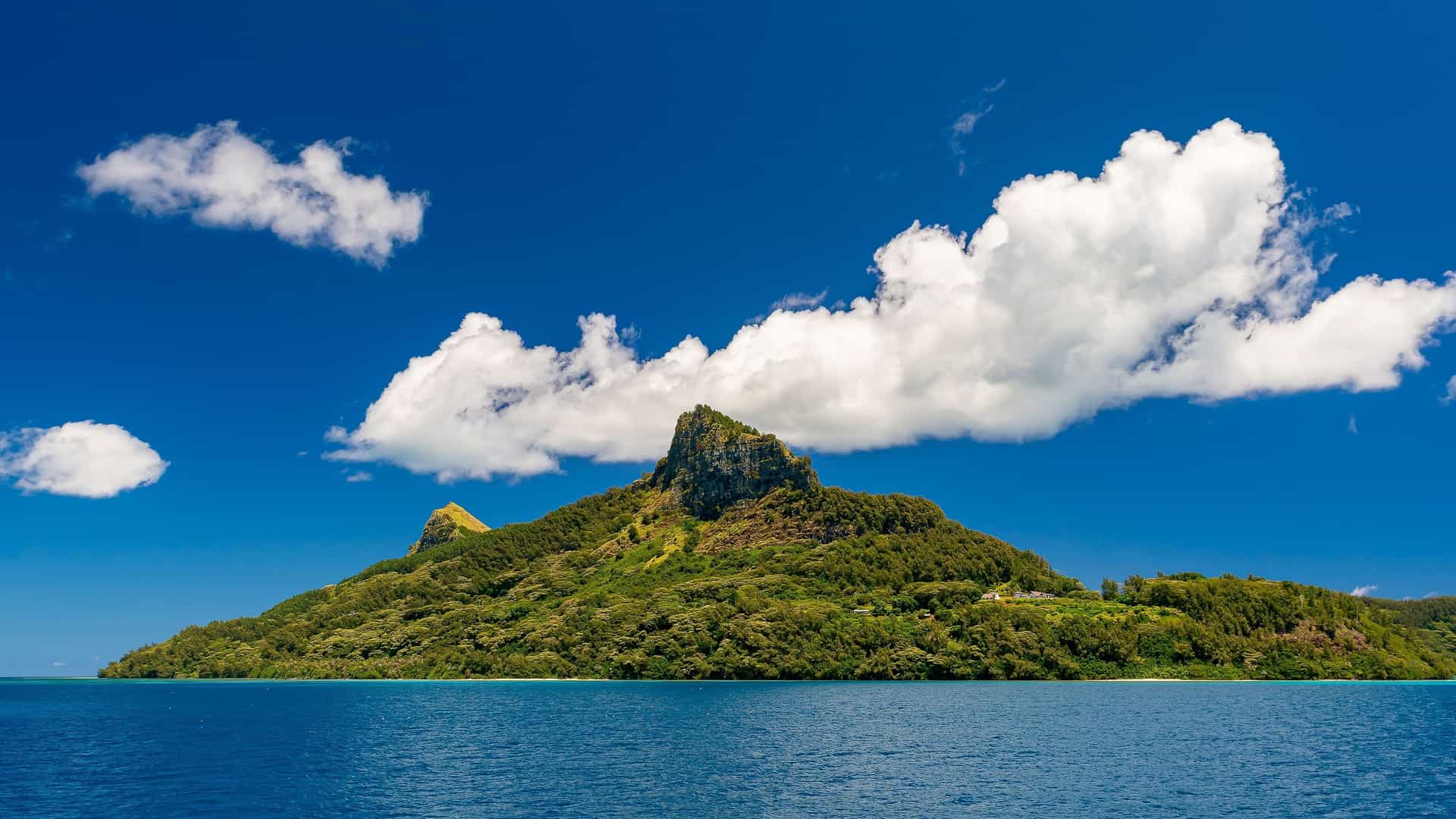 A beautiful shot of the volcanic peaks of Mangareva Island in the Gambier Islands, French Polynesia, rising from the turquoise waters of the lagoon under a blue sky.