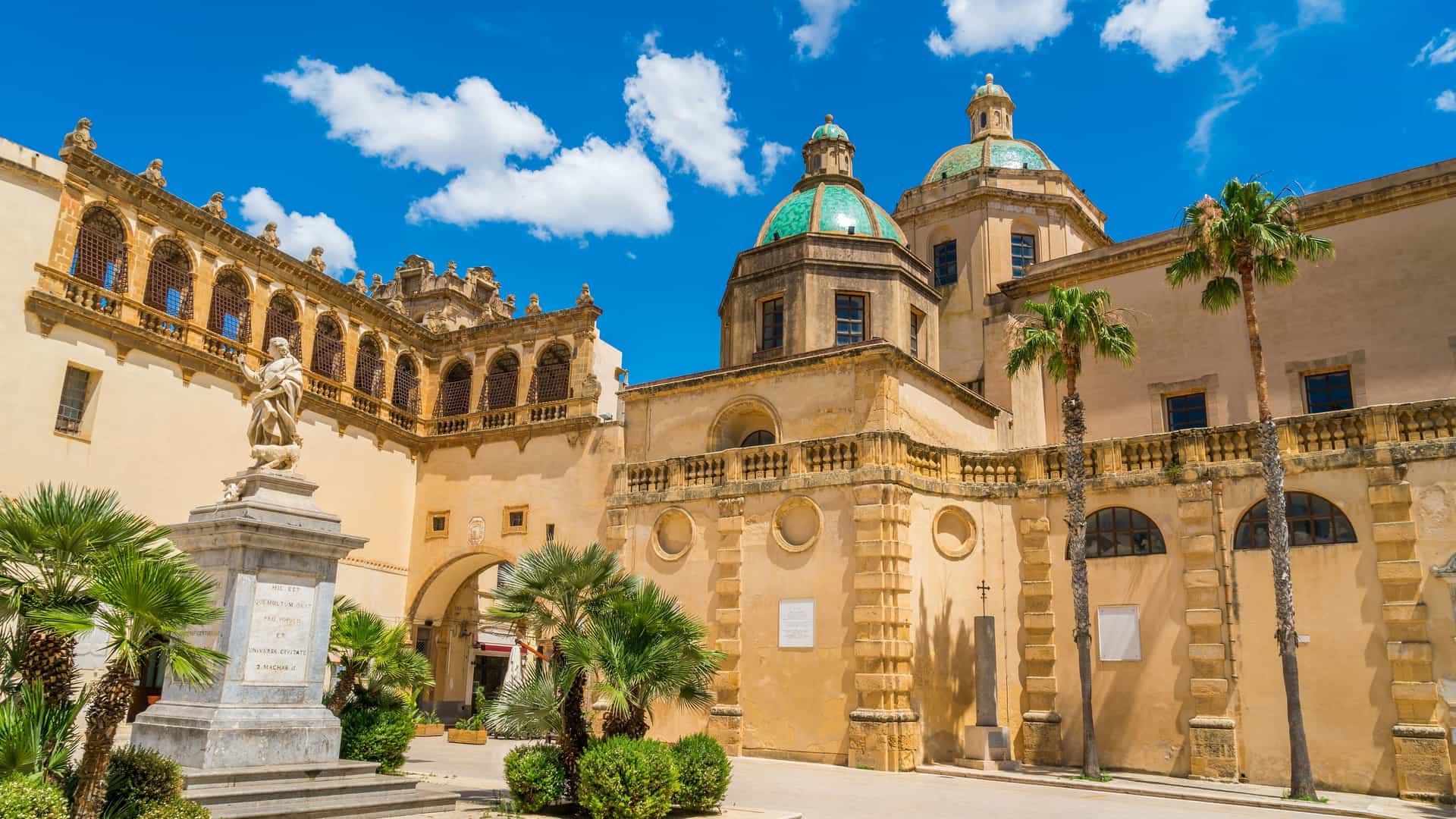 "A vibrant street view of the historic Piazza della Repubblica in Mazara del Vallo, Italy, showcasing the baroque Church of San Vito in Mazara and the seminary building under a bright blue sky.  "