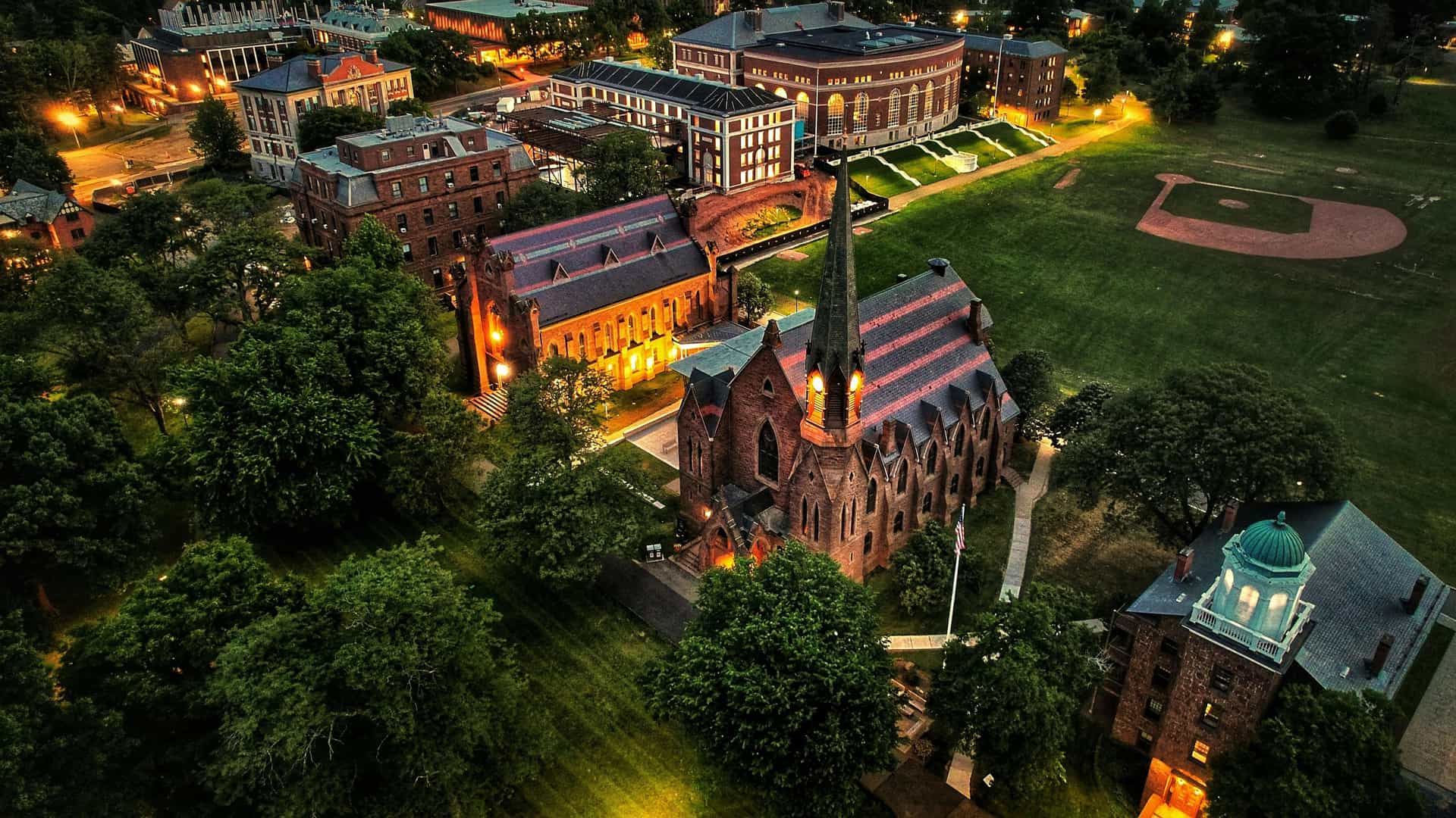 "An aerial dusk view of the Wesleyan University campus in Middletown, Connecticut, with the historic Memorial Chapel and surrounding buildings lit up at night.  "