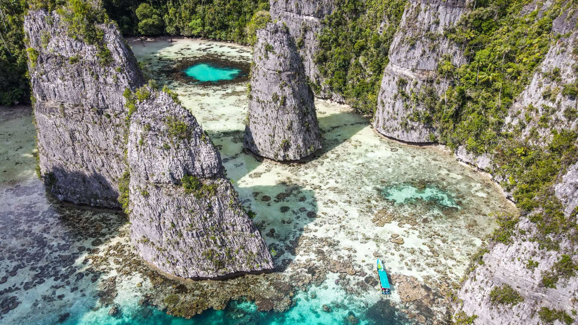 An aerial view of the iconic rock formations and turquoise lagoons of Misool Island, Raja Ampat, Indonesia, showcasing a vibrant coral reef and a small boat navigating the stunning landscape.