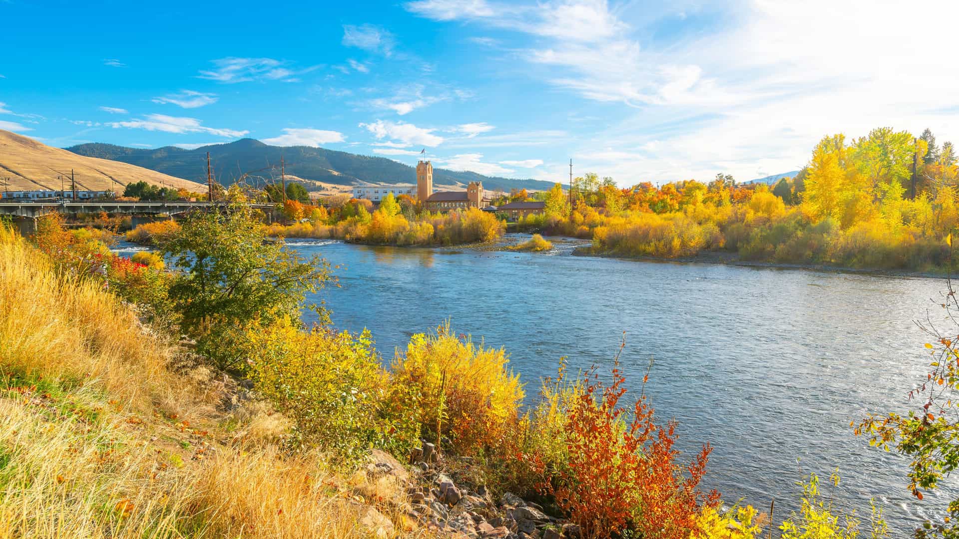 "A stunning autumn view of the Clark Fork River in Missoula, Montana, with the historic Milwaukee Depot in the background and vibrant yellow foliage along the riverbank.  "