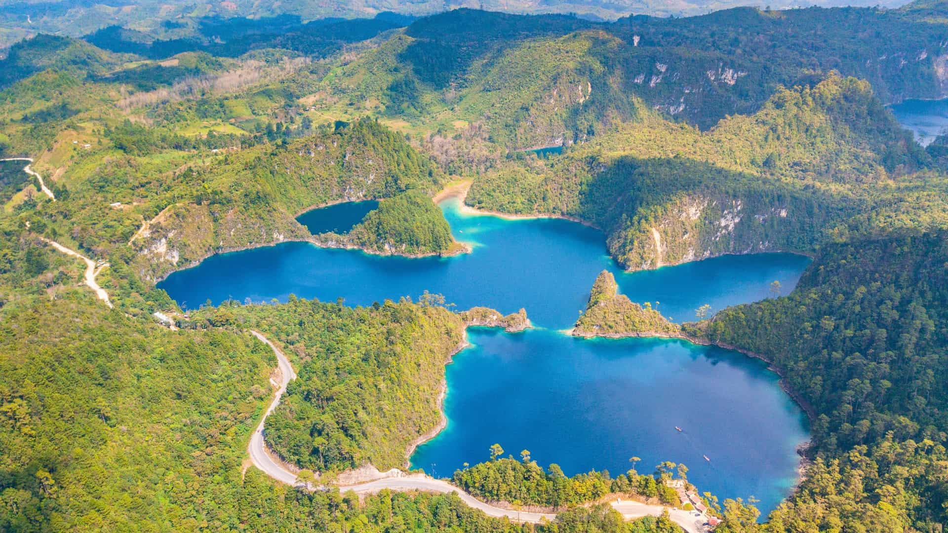 An aerial view of the Montebello Islands Marine Park, Australia, showcasing a cluster of beautiful blue lakes nestled within a lush, green landscape of forested hills and valleys.