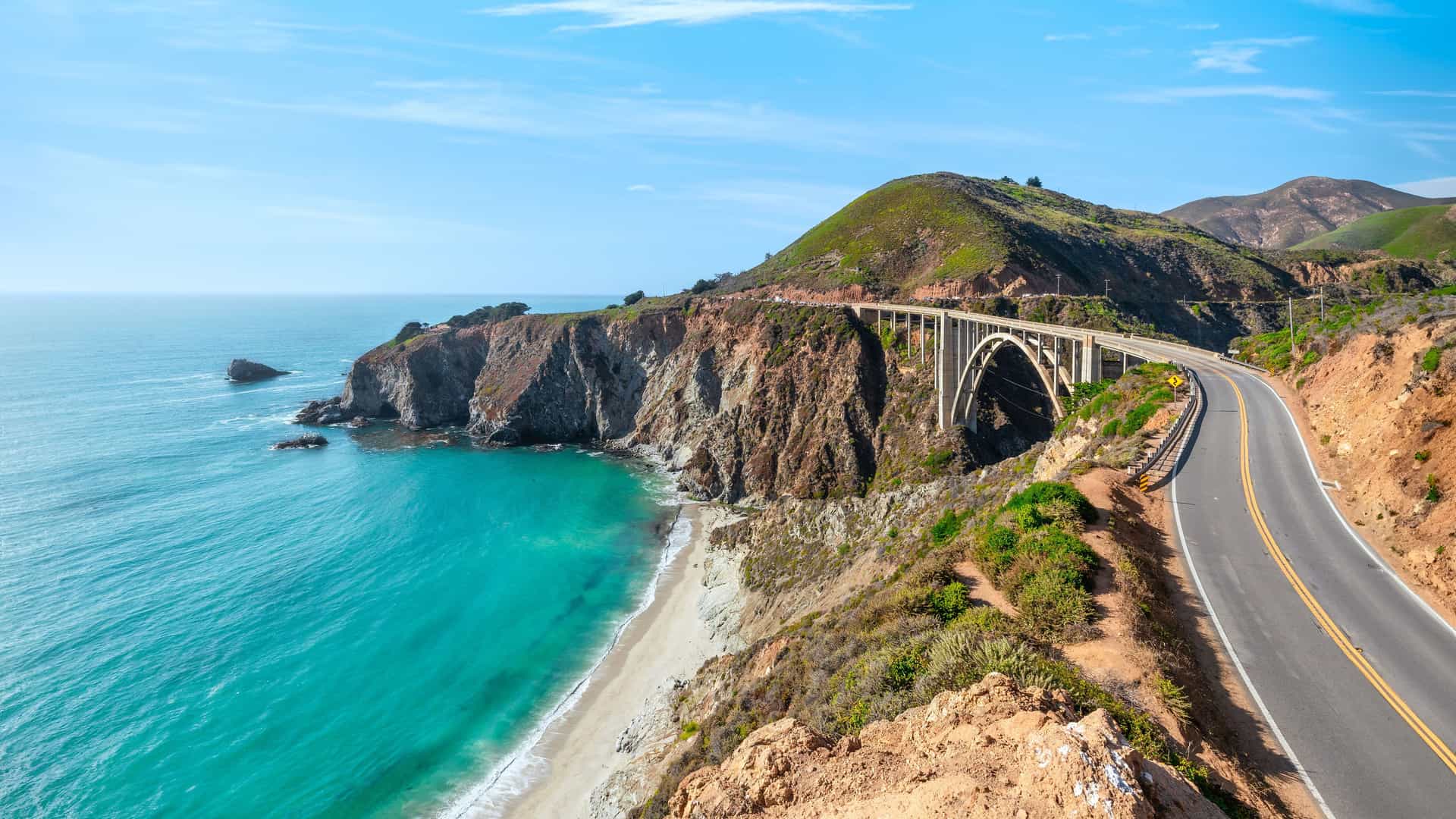 "A high-angle scenic view of the iconic Bixby Bridge in Monterey, California, spanning a coastal gorge along the beautiful Pacific Coast Highway.  "