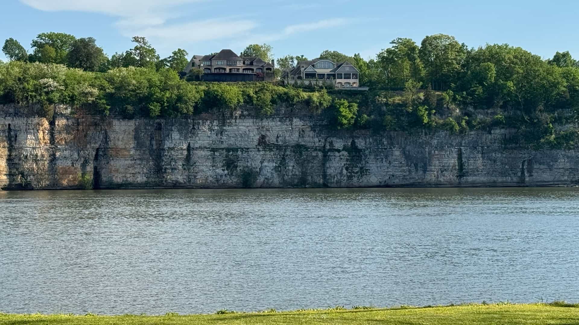 Houses stand on a lush, forested bluff overlooking a prominent limestone cliff and the water in the Muscle Shoals Area, Alabama.