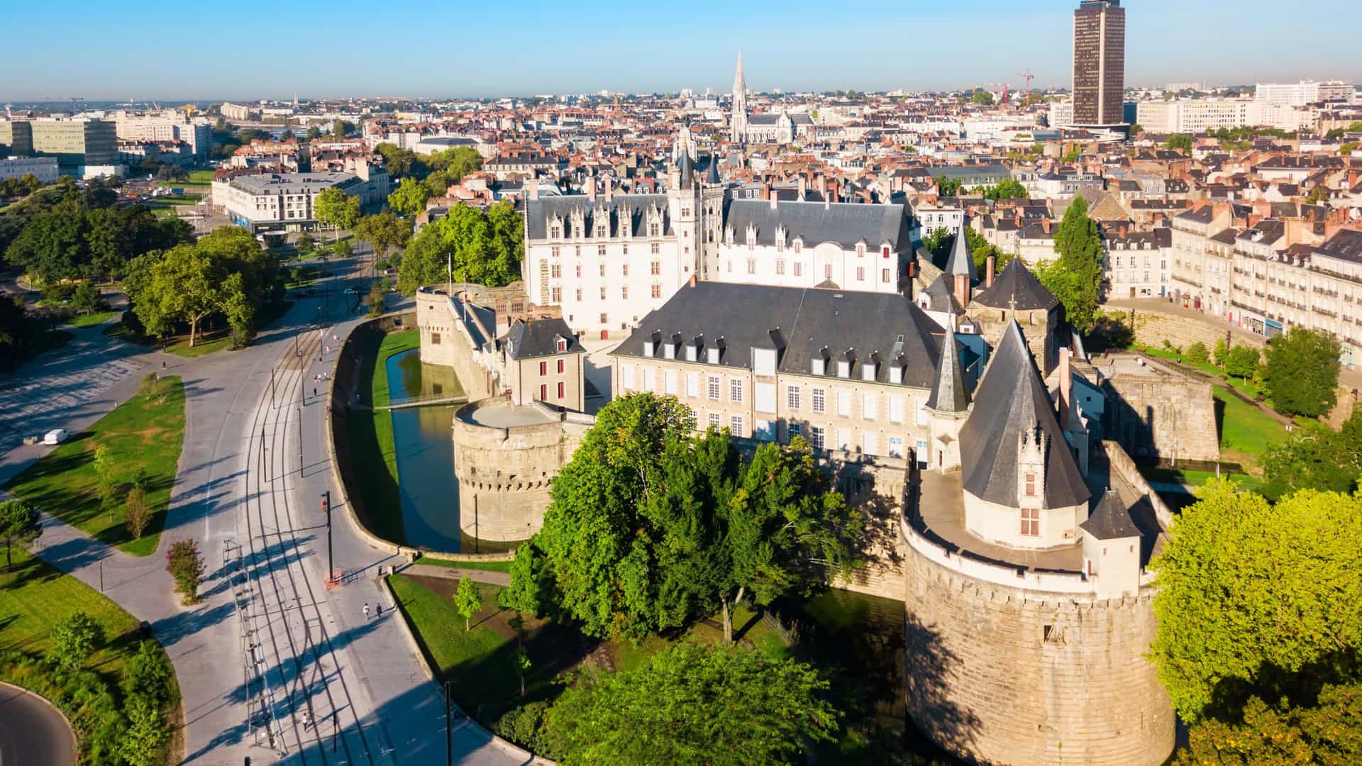 "An aerial view of the historic city of Nantes, France, with the medieval Château des Ducs de Bretagne (Castle of the Dukes of Brittany) in the foreground and the city skyline in the background.  "