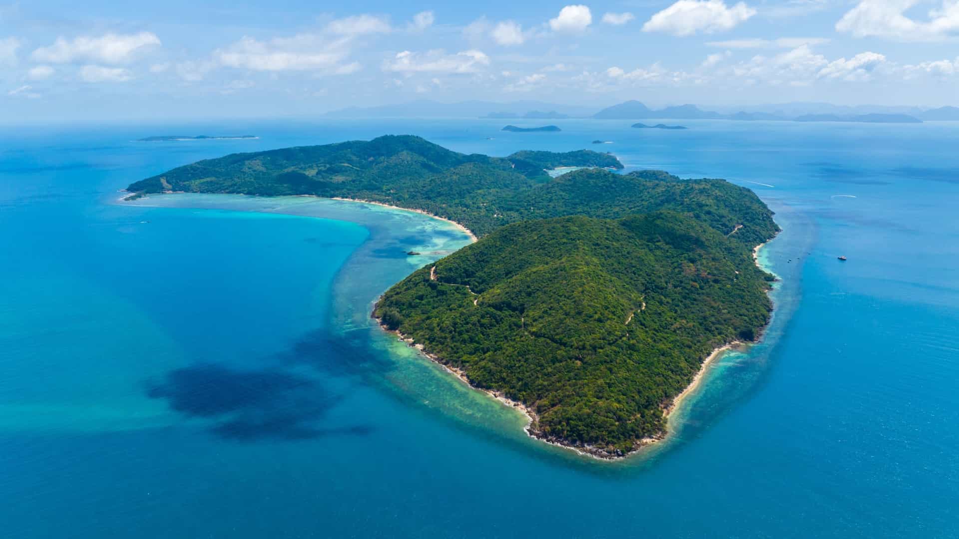 An aerial view of a lush, green, forested island surrounded by the deep blue and clear turquoise waters near Nathon, Thailand.