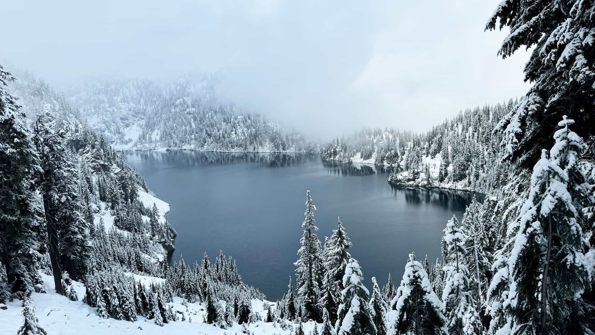 "A stunning panoramic shot of a serene winter landscape at Snow Lake, a popular hiking trail near North Bend, Washington, covered in fresh snow.  "
