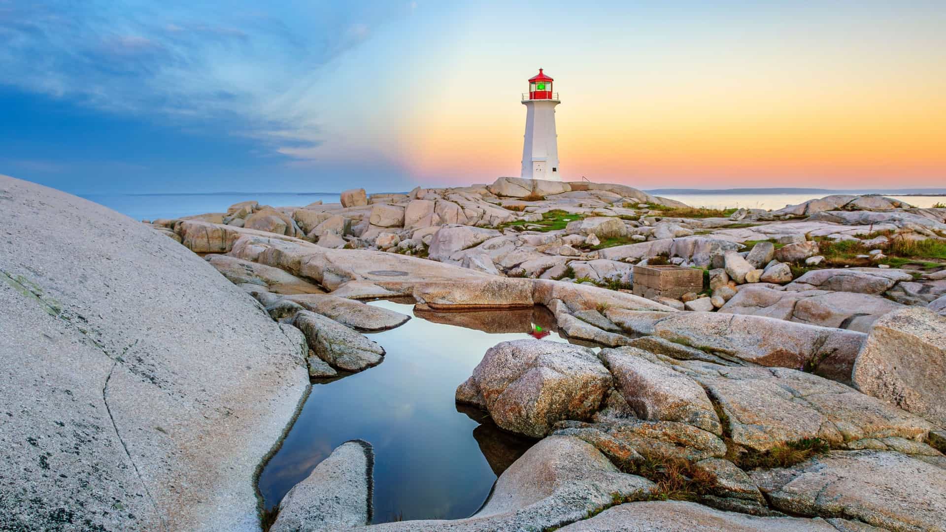 A scenic sunset view of the iconic Peggy's Cove Lighthouse in Nova Scotia, Canada, standing on a rocky shoreline with small tide pools.