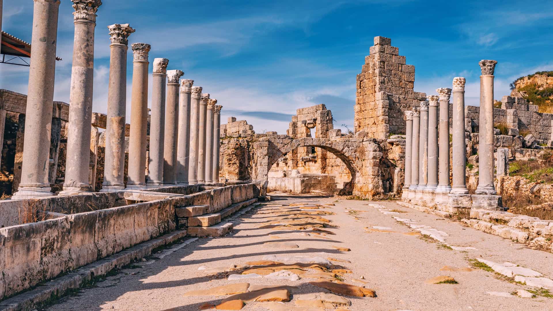"A scenic shot of the ancient ruins of the Temple of Olympian Zeus in Olympia, Greece, showing a row of massive stone columns under a bright blue sky.  "