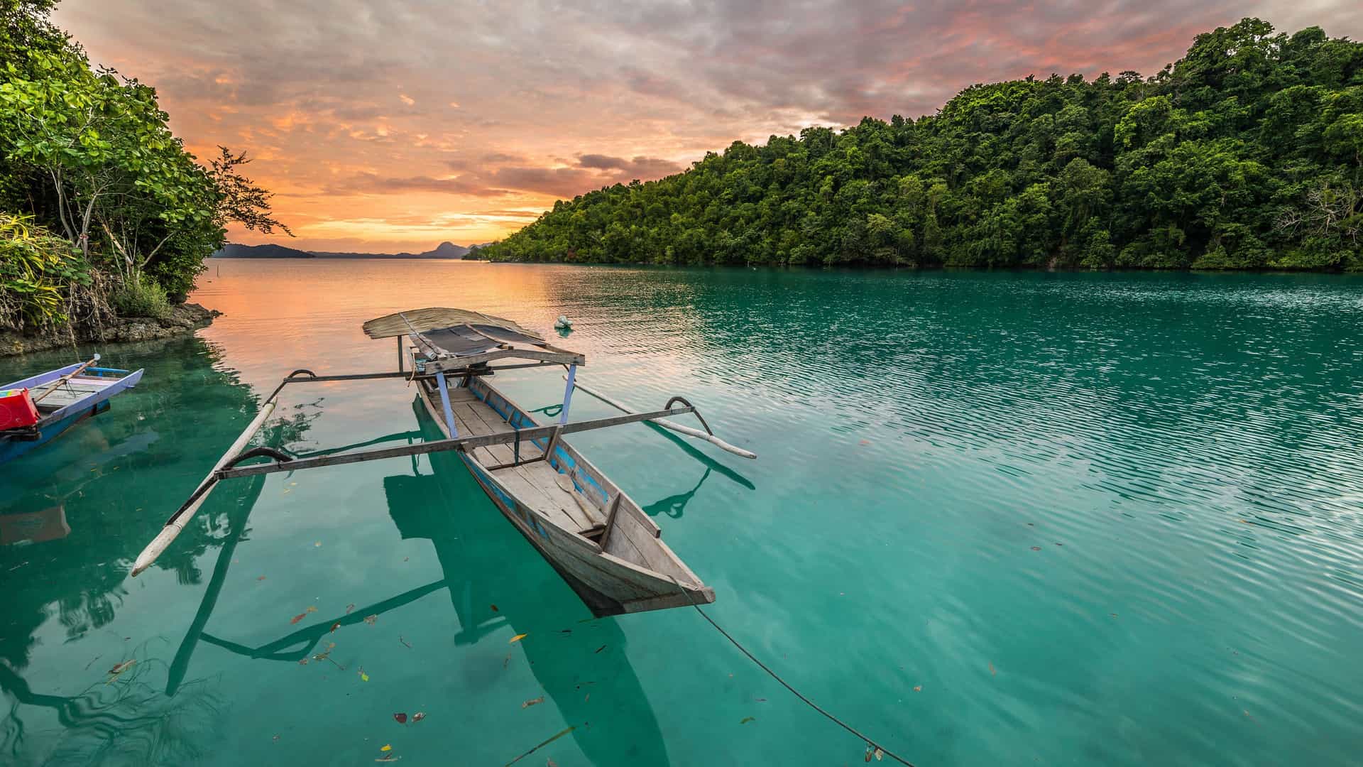 A stunning view of an outrigger fishing boat floating in the clear turquoise water of Palopo, a port city in Sulawesi, Indonesia, at sunrise.