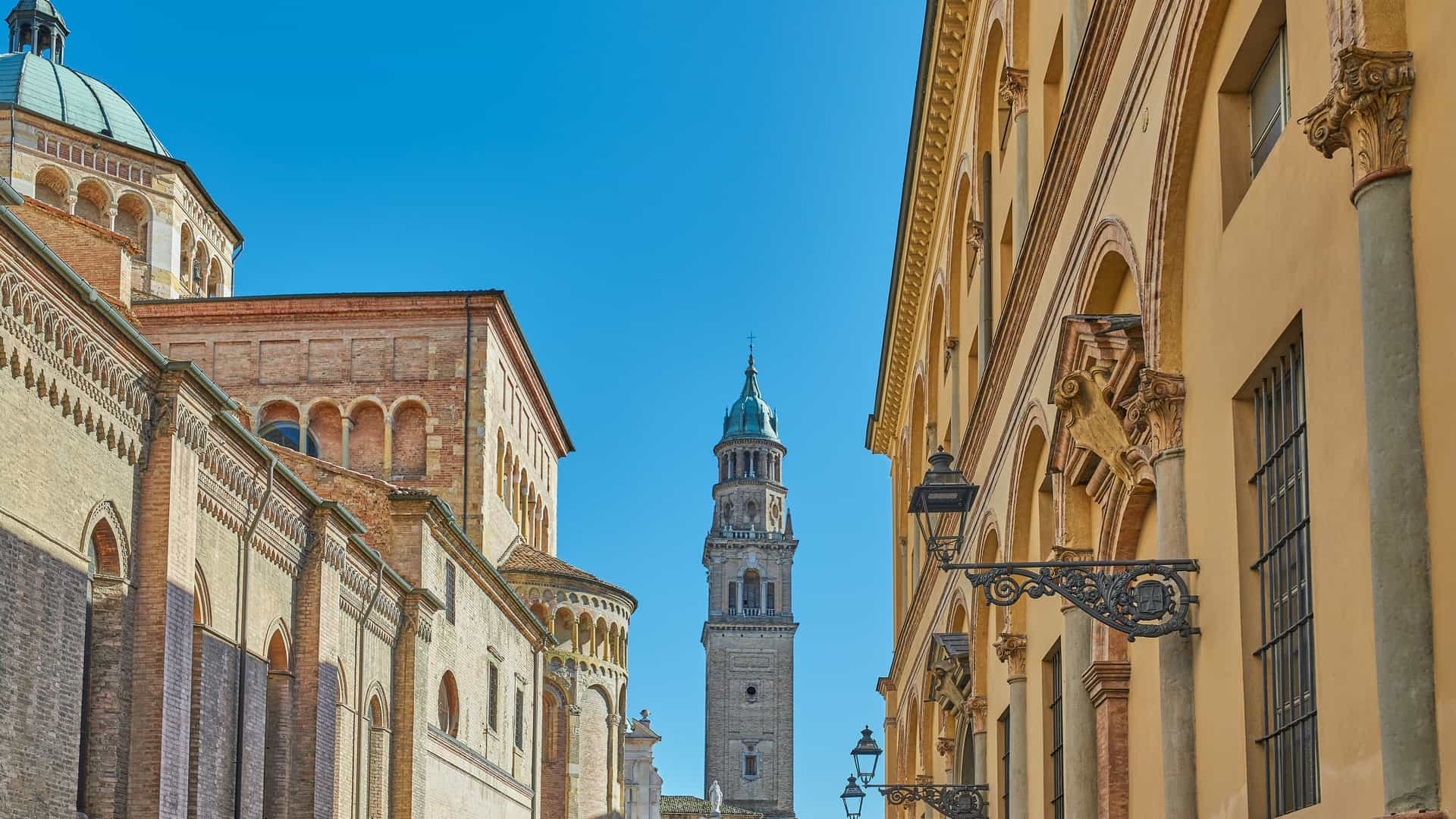 "A stunning low-angle shot of the historic Parma Cathedral and its towering bell tower, the Campanile, visible between two old buildings in Parma, Italy.  "