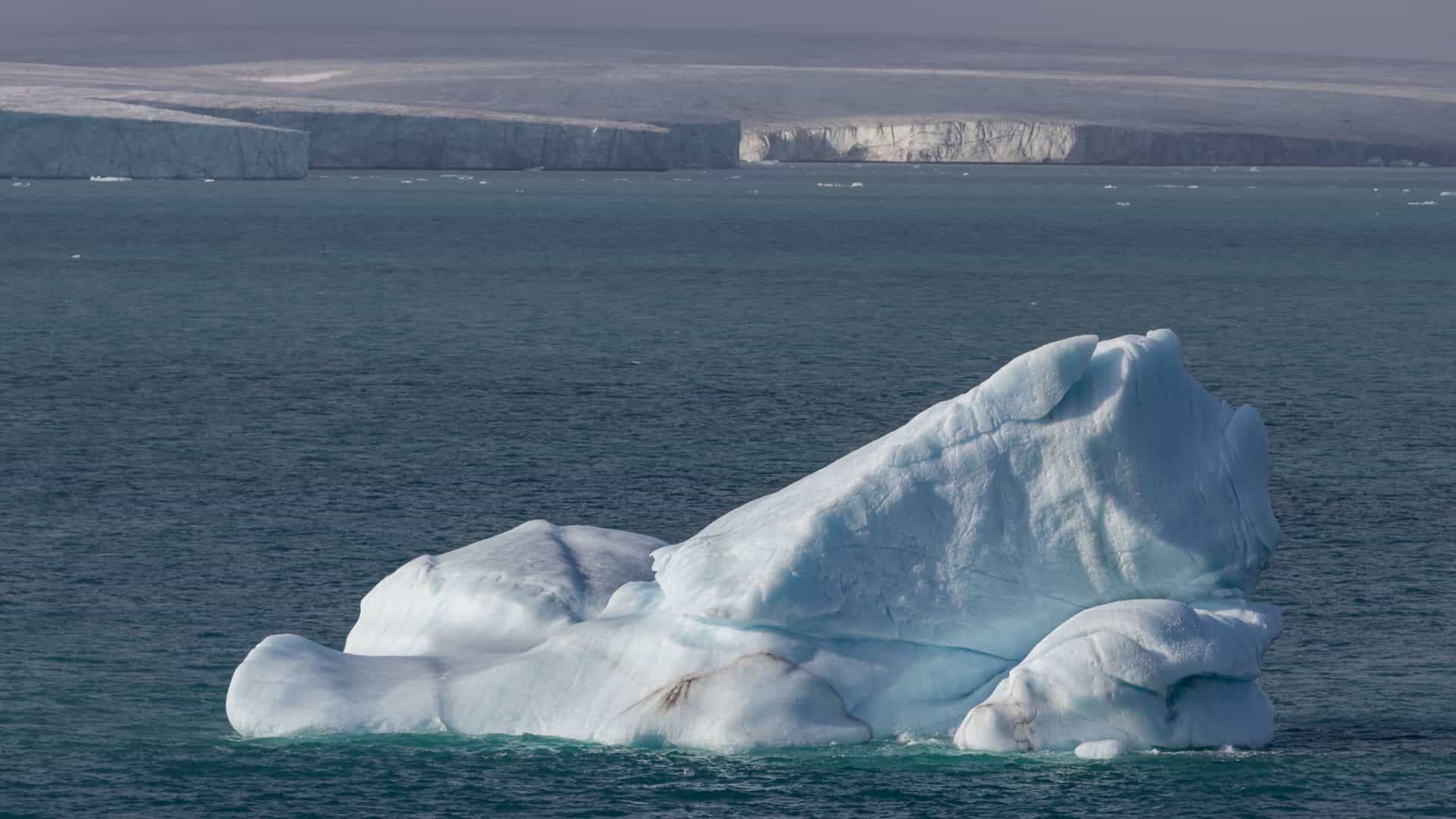 A close-up view of a large iceberg floating in the frigid water near Philpots Island, Nunavut, with a huge glacier wall in the background.