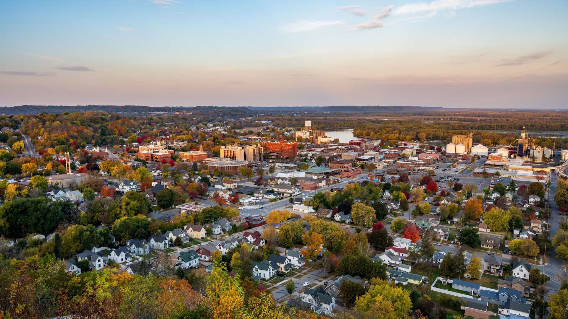 An aerial view of the small town of Red Wing, Minnesota, with colorful autumn foliage surrounding residential homes and the downtown area along the Mississippi River.