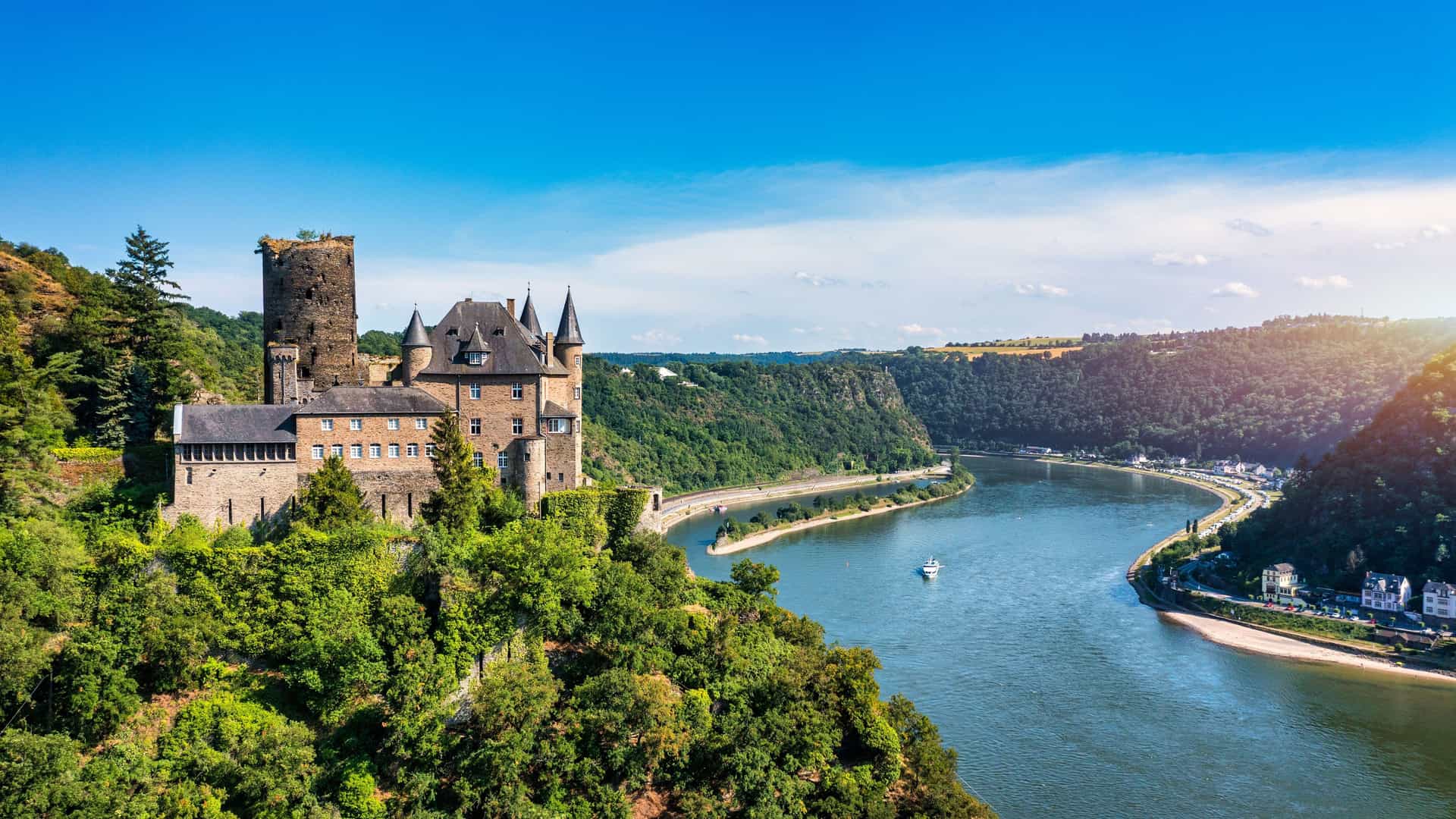 "A scenic view of a medieval German castle with turrets and towers, perched on a hill overlooking the Rhine River, a popular cruise destination in Rhineland.  "