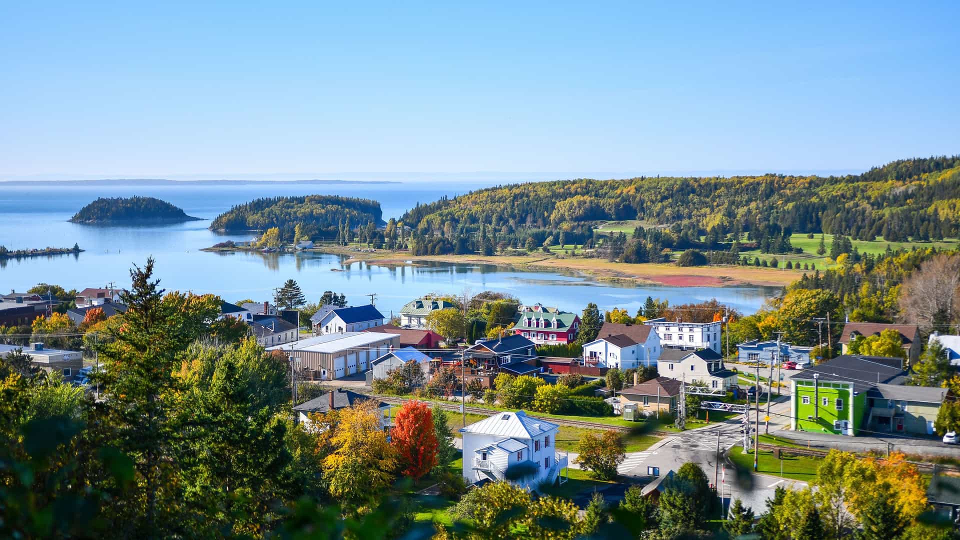 "A picturesque village on the water's edge in Rimouski, Canada, with colorful houses surrounded by lush green forests in the beautiful Bas-Saint-Laurent region.  "