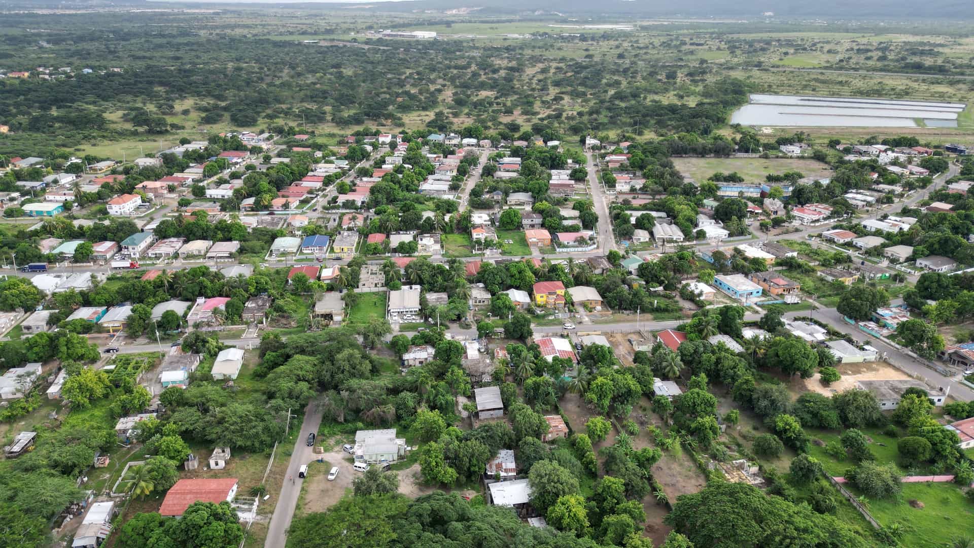 An aerial view of Spanish Town, Jamaica, with a dense cluster of residential houses and lush green trees and foliage in a rural setting.