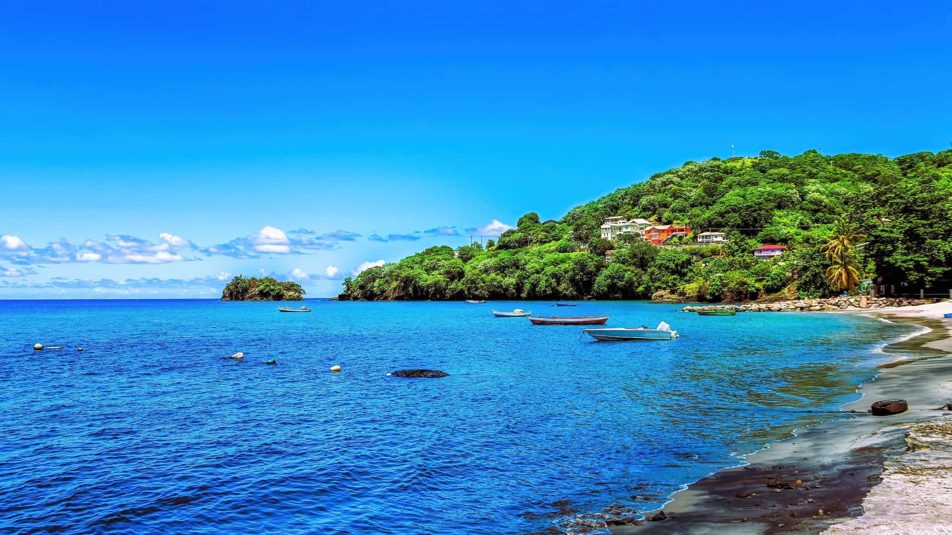 A scenic Caribbean bay near Kingstown, Saint Vincent and the Grenadines, with small boats anchored in the turquoise water and lush green hillsides with colorful houses.