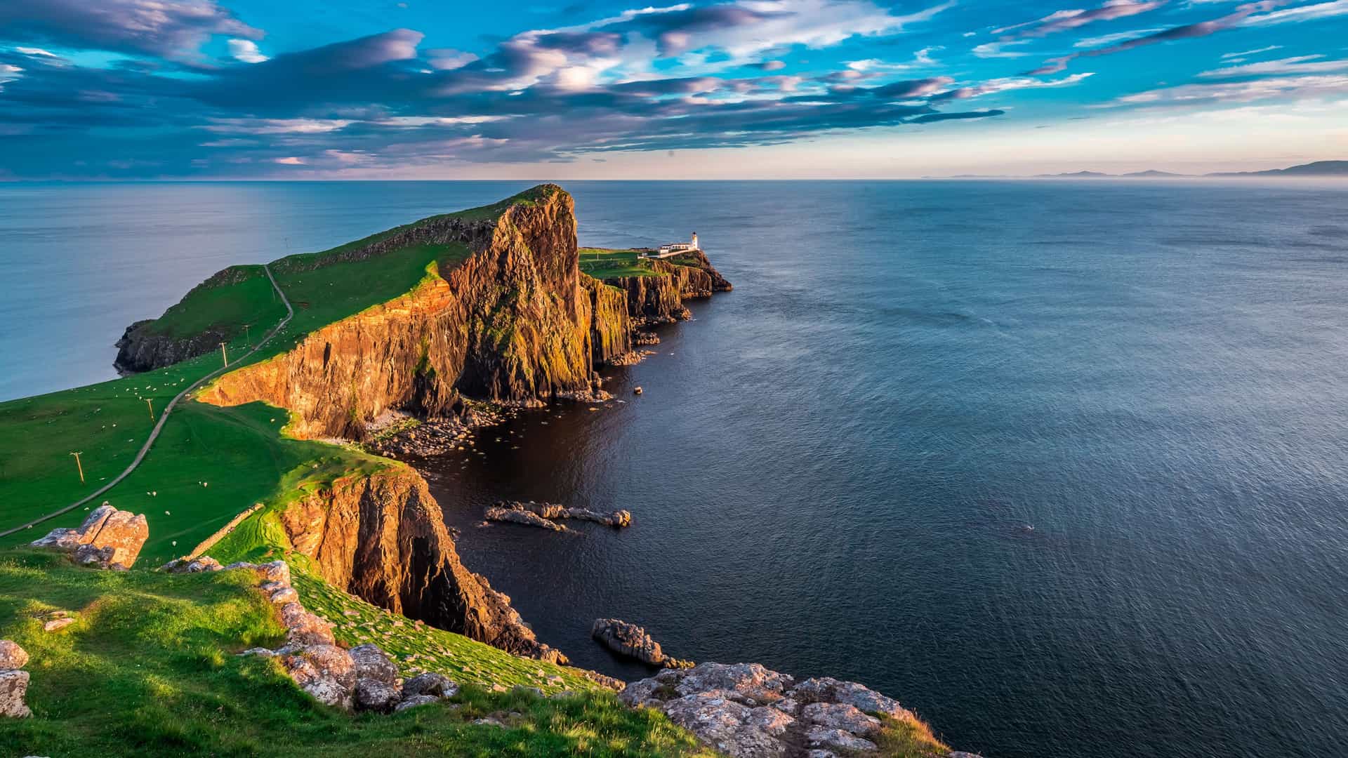A scenic view of a rugged, rocky cliffside landscape on the island of Tanera Beag in Scotland, with a lighthouse and walking path along the cliff's edge.