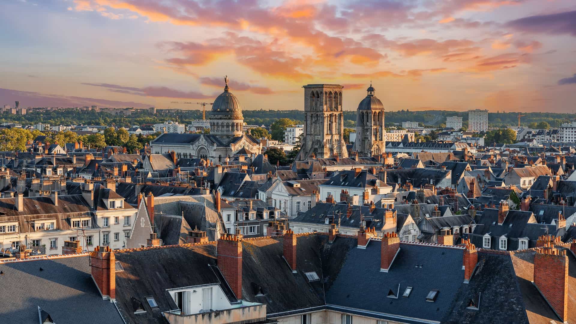 A stunning aerial view of the historic city of Tours, France, with its distinctive rooftops and cathedral steeples silhouetted against a beautiful sunset sky.