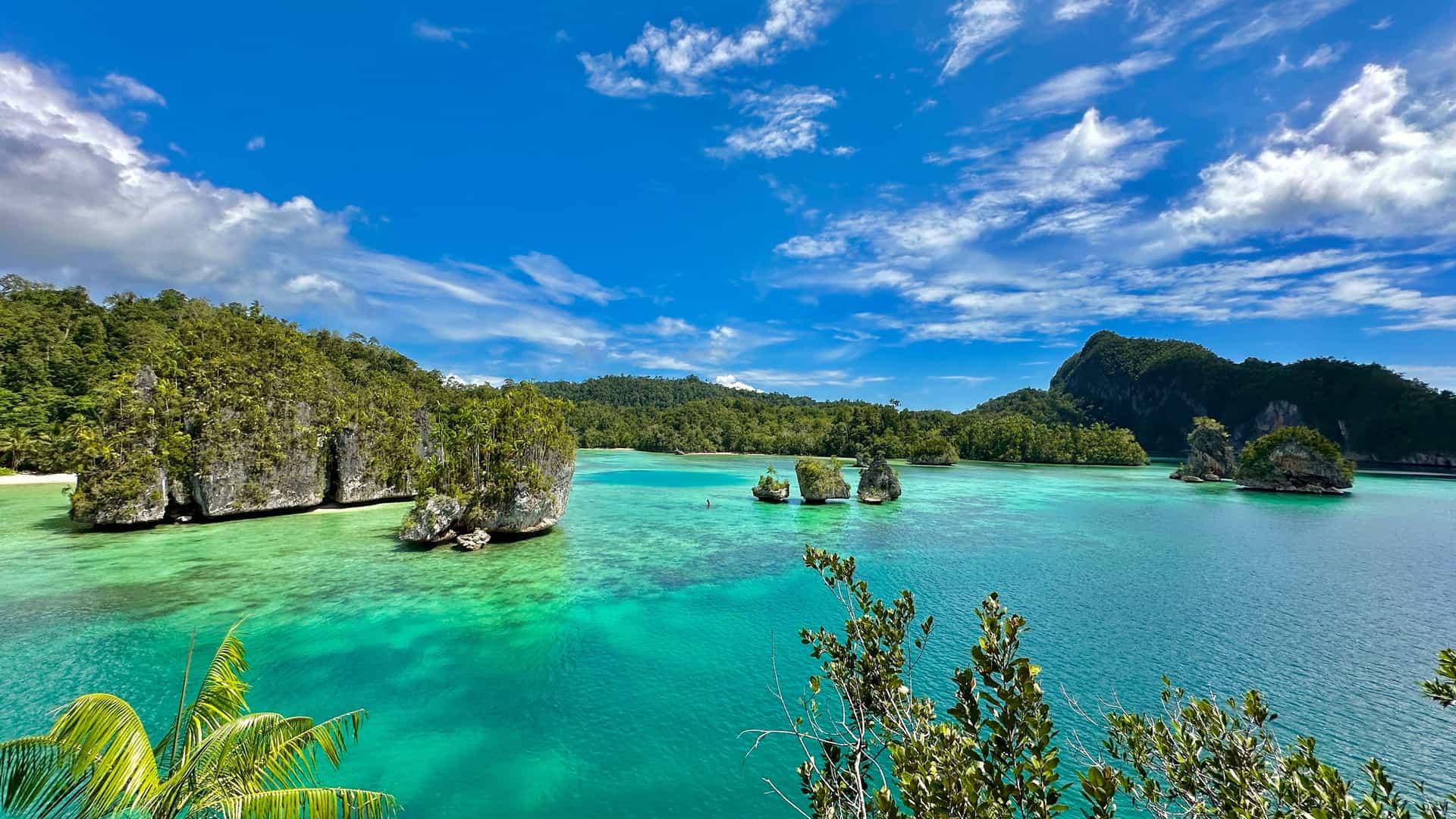 A beautiful view of Triton Bay in West Papua, Indonesia, with a clear turquoise sea, lush green limestone islands, and a perfect blue sky.