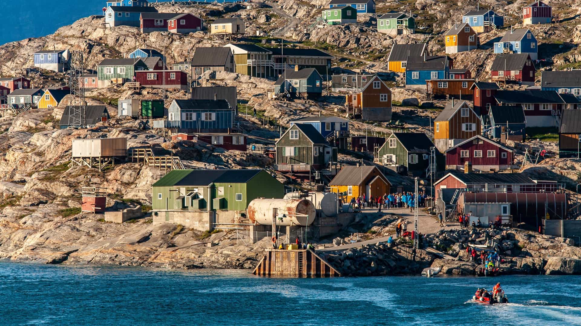 Colorful homes are clustered on the rocky hillside above a small dock and boat in the remote settlement of Uummannaq, Greenland.