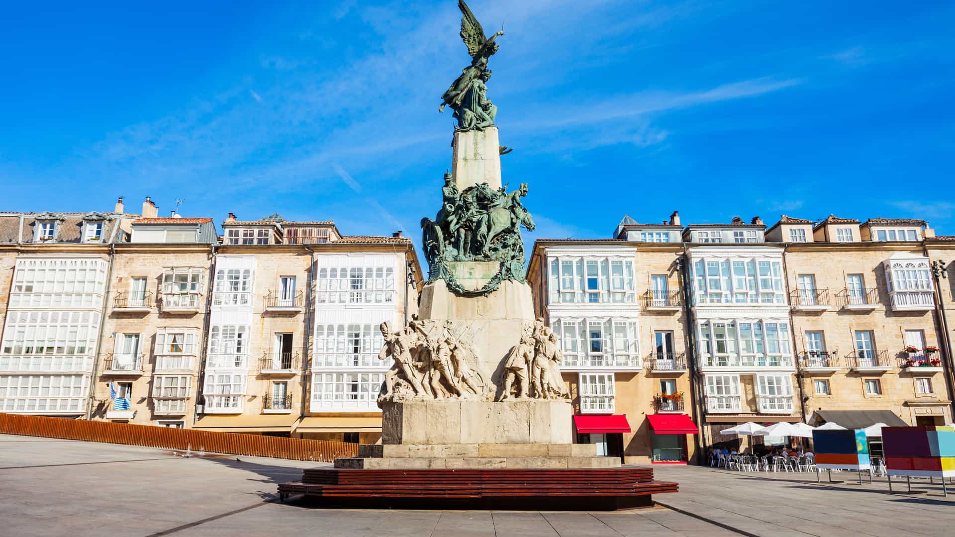 "A bronze monument of a winged figure on horseback atop a stone base, standing in the center of a wide city square with historic buildings in Vitoria-Gasteiz, Spain.  "