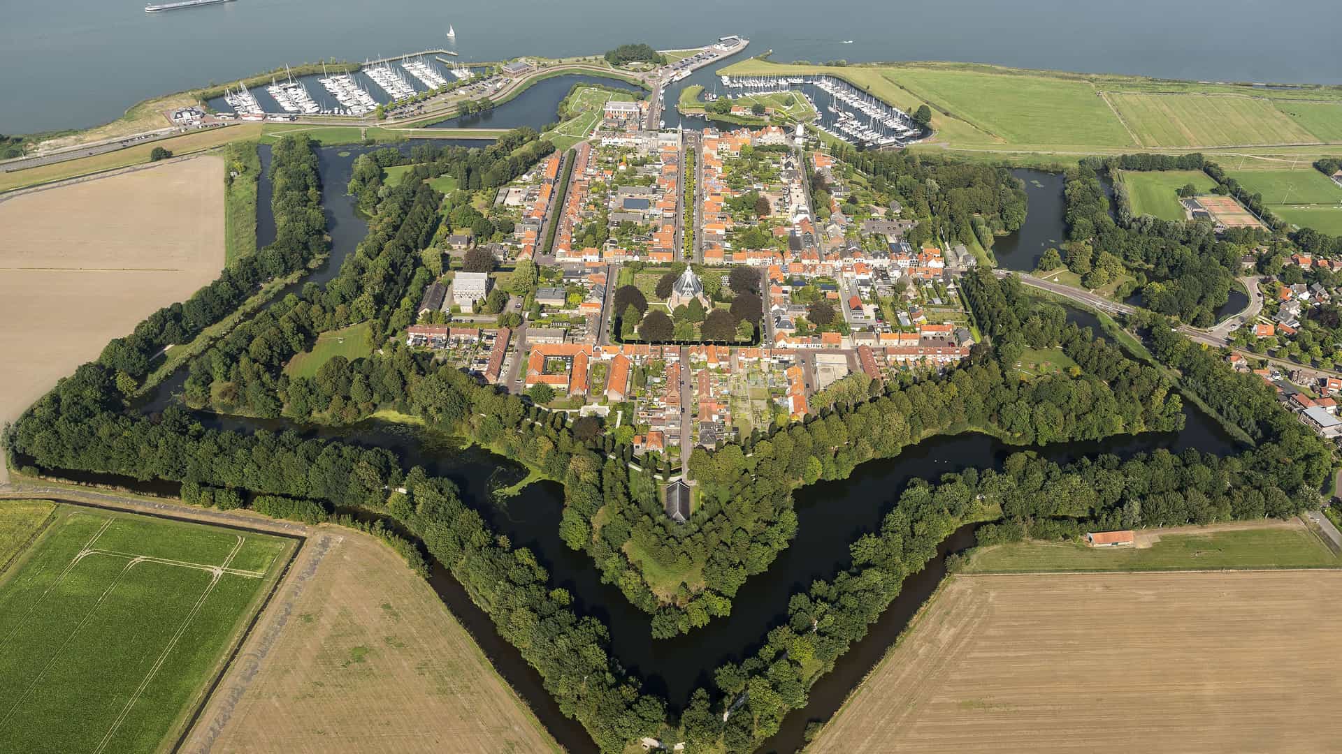 "An aerial view of the historic star-shaped fortress town of Willemstad, the Netherlands, surrounded by a moat and lush green fields.  "