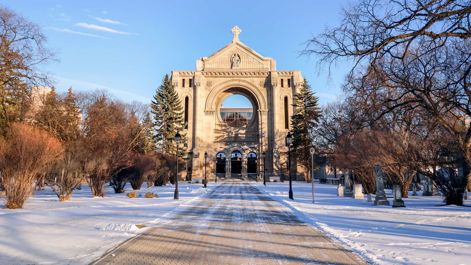 "A stunning winter view of the historic St. Boniface Cathedral-Basilica in Winnipeg, Canada, with a wide, snow-covered pathway leading to the iconic stone facade.  "