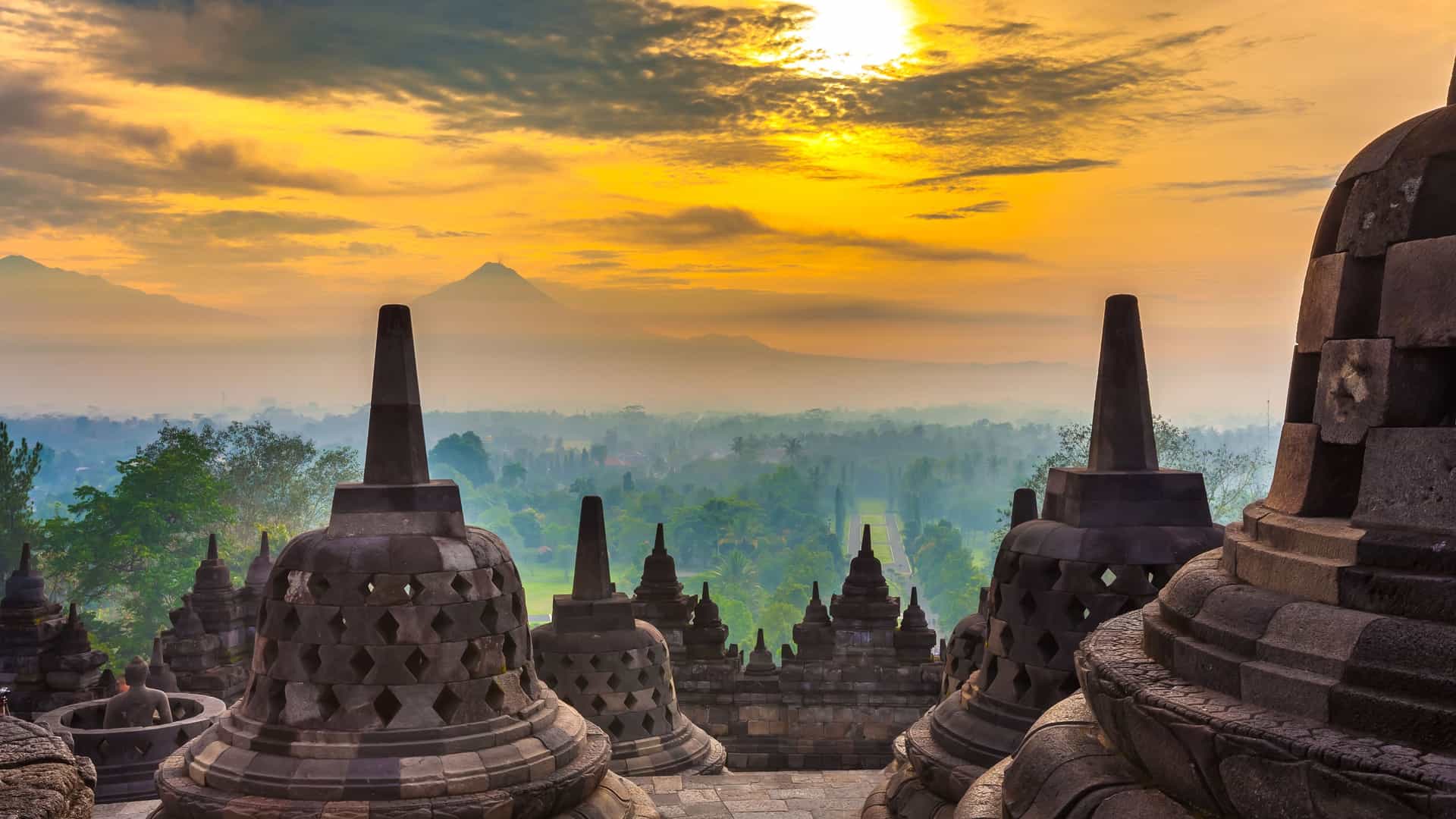 "A serene sunrise view over the ancient Borobudur Temple in Yogyakarta, Indonesia, with its stone stupas and carvings, overlooking a misty valley and a distant volcano."