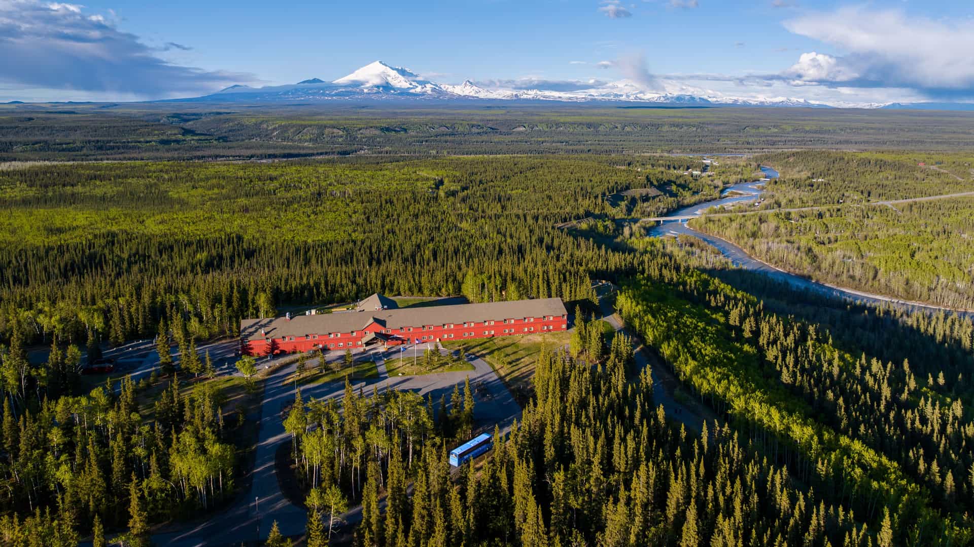 An aerial drone shot of Copper River Princess Wilderness Lodge showing the secluded-wilderness that surrounds the lodge with mountains in the background.